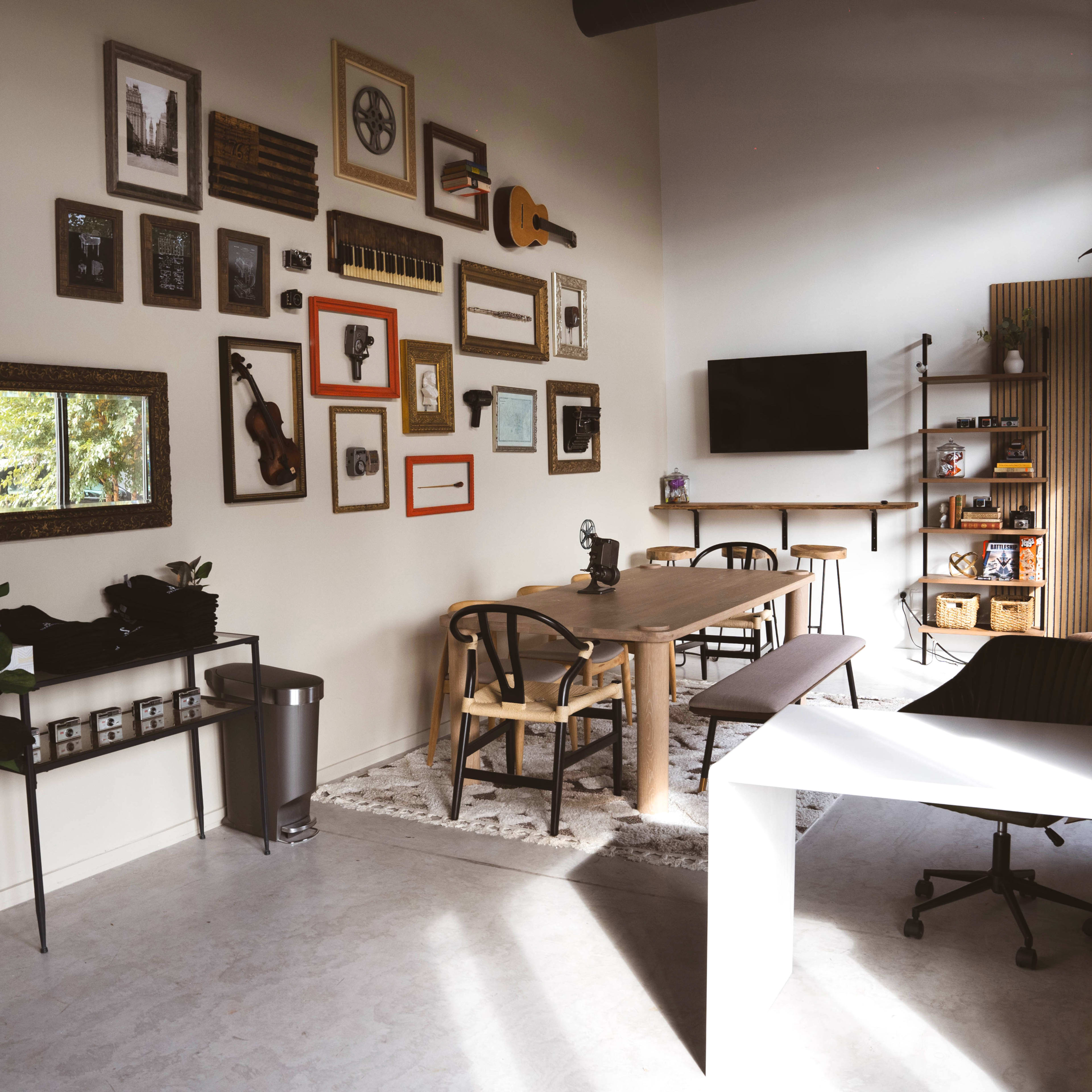 A modern workspace featuring a wooden table surrounded by chairs, adorned with framed artwork and a television on the wall.