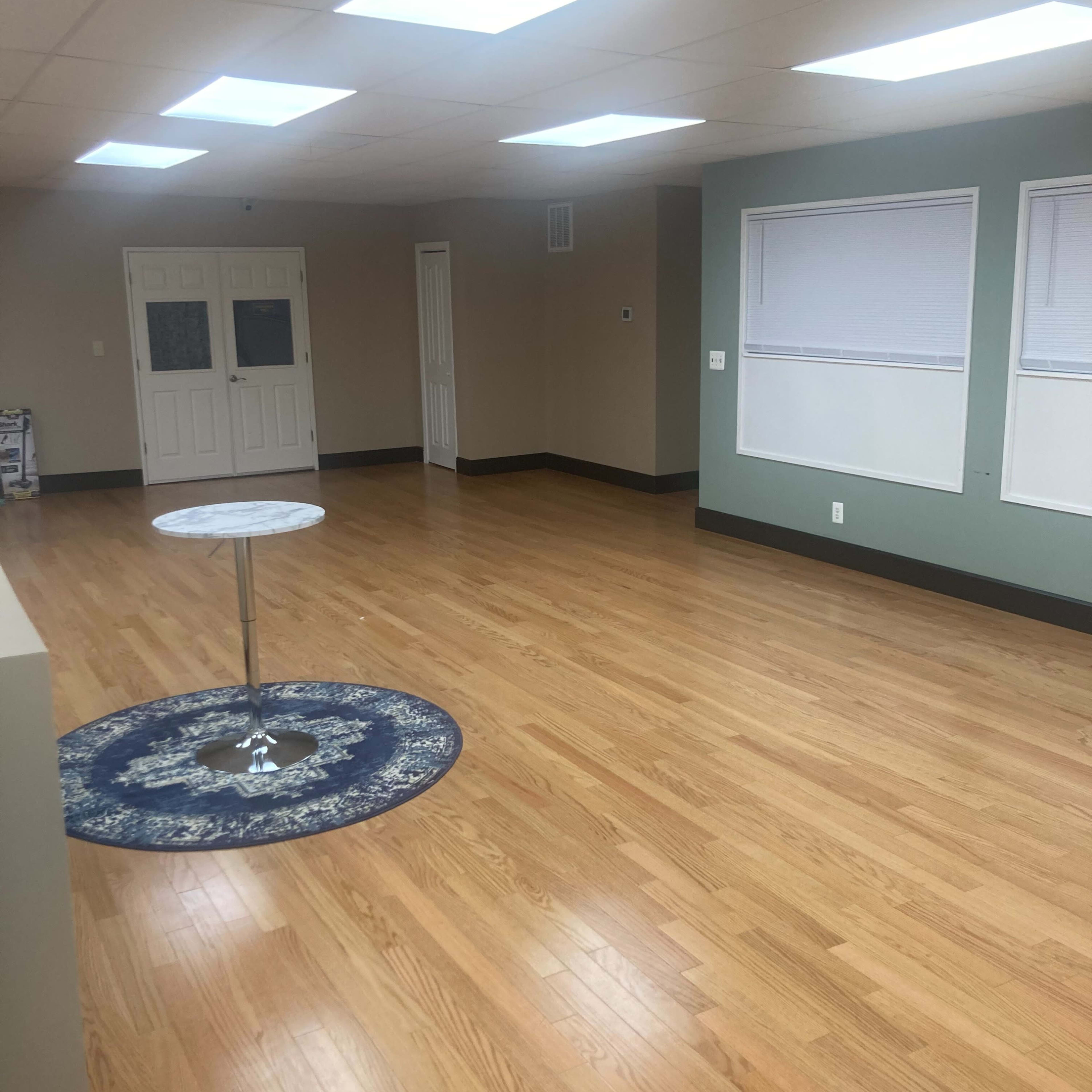 A spacious, empty room with hardwood flooring, a circular rug in the center, and overhead skylights providing natural light.