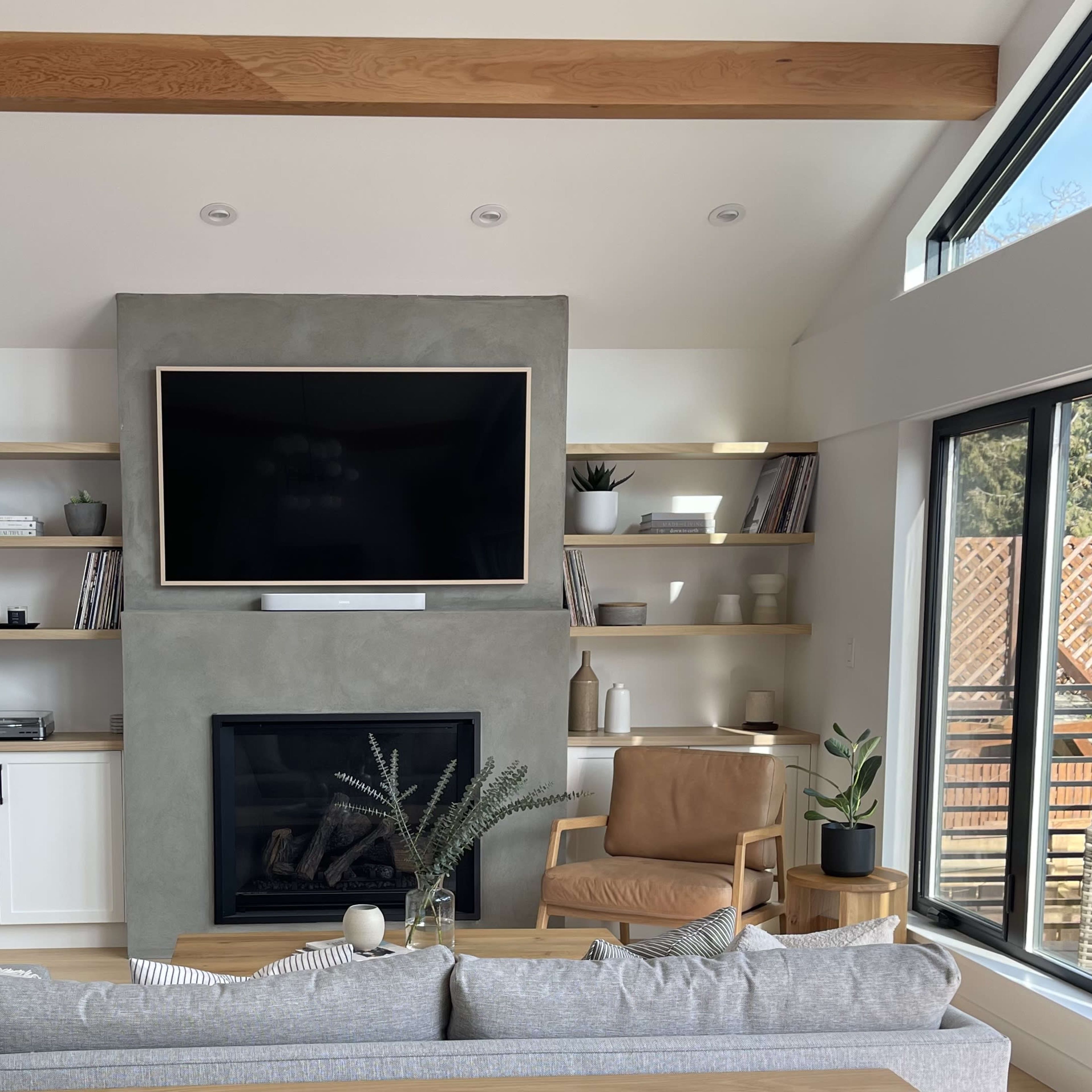 A modern living room featuring a large flat-screen TV mounted above a minimalist fireplace, flanked by wooden shelves filled with decorative items and books.