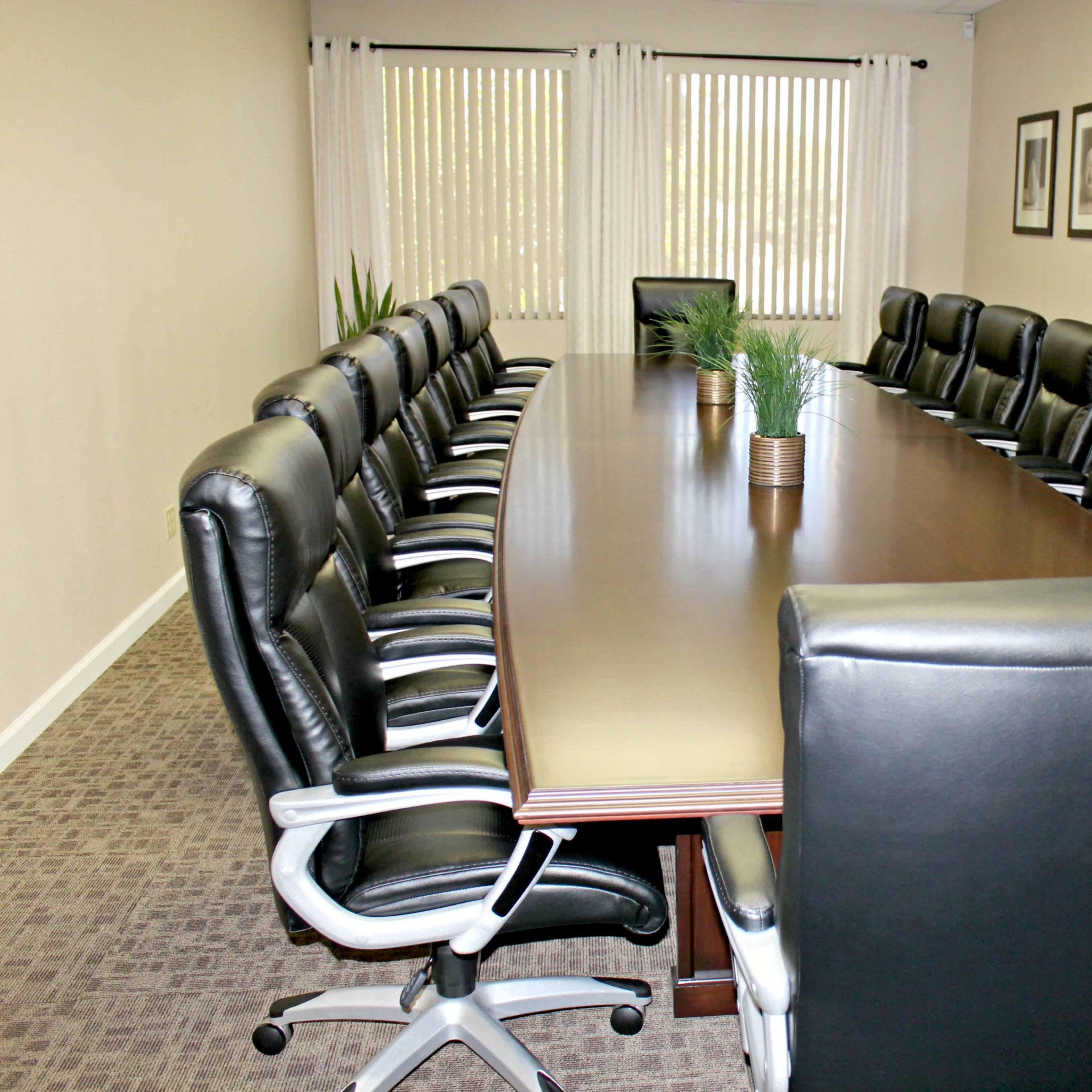 A large conference room features a long wooden table surrounded by black leather chairs and decorated with framed artworks on the walls.