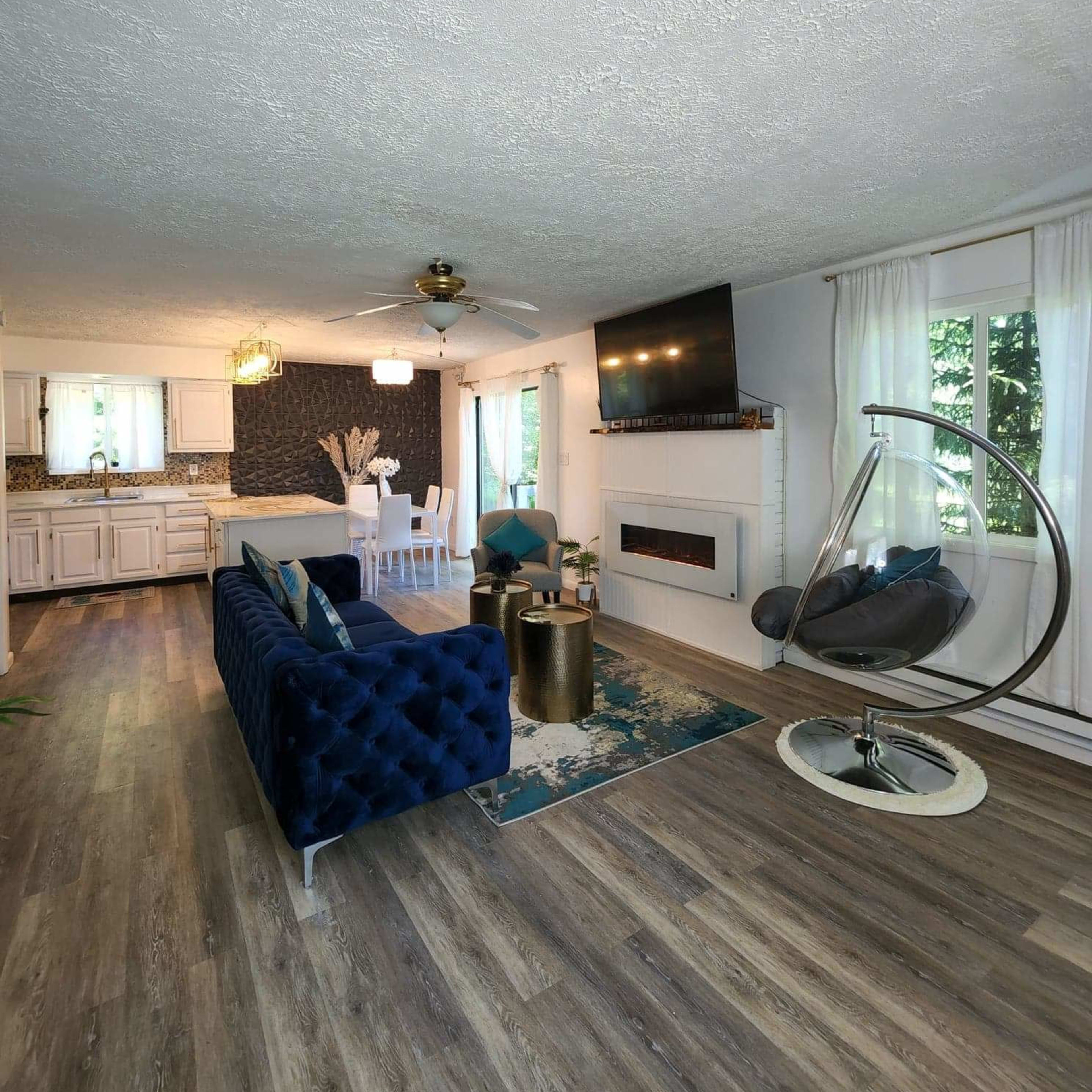 A modern living room featuring a blue velvet sofa, a hanging chair, and a flat-screen TV mounted above an electric fireplace.
