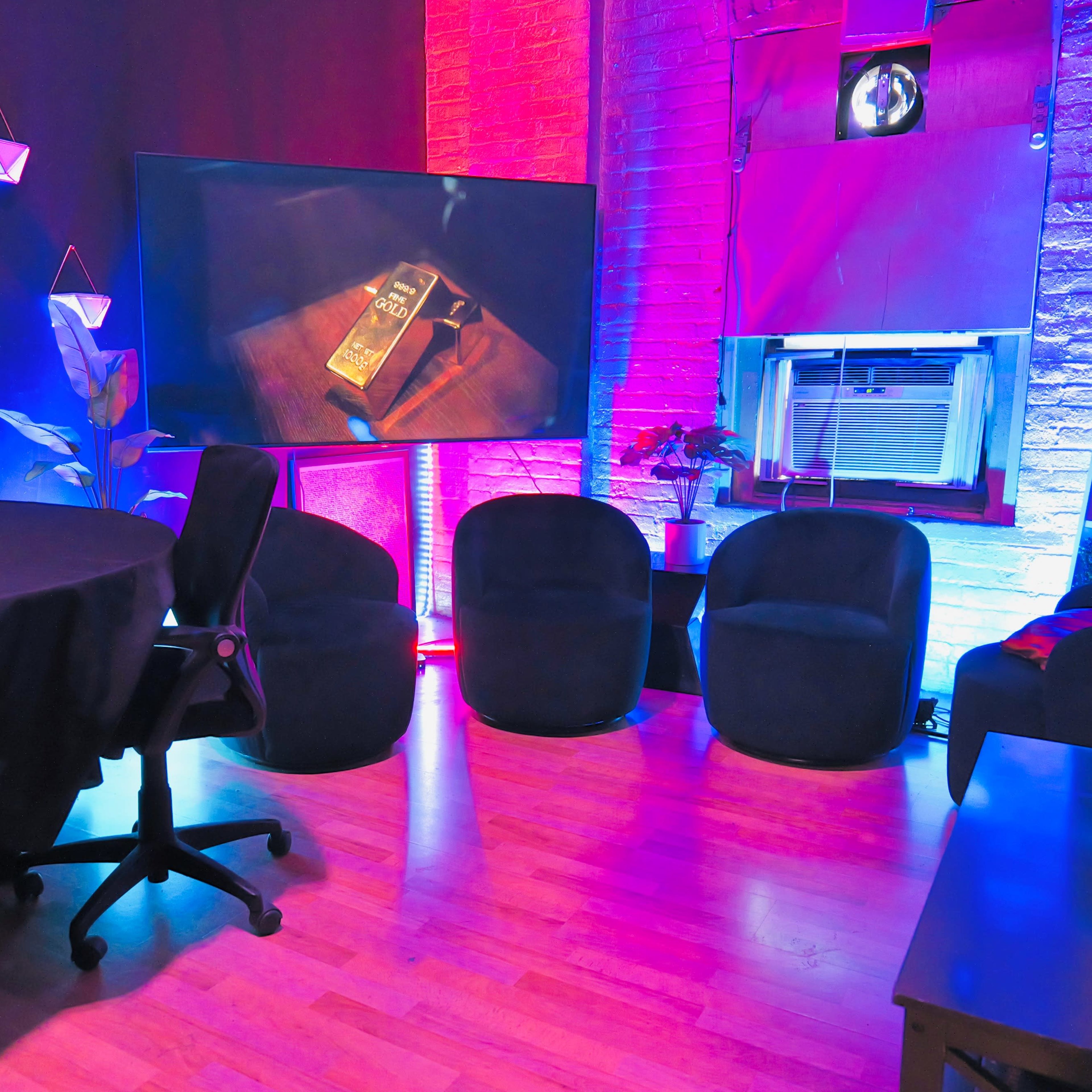 A modern indoor space featuring a round table, four black armchairs, and a large screen displaying a book, with colorful lighting and decorative elements on the walls.