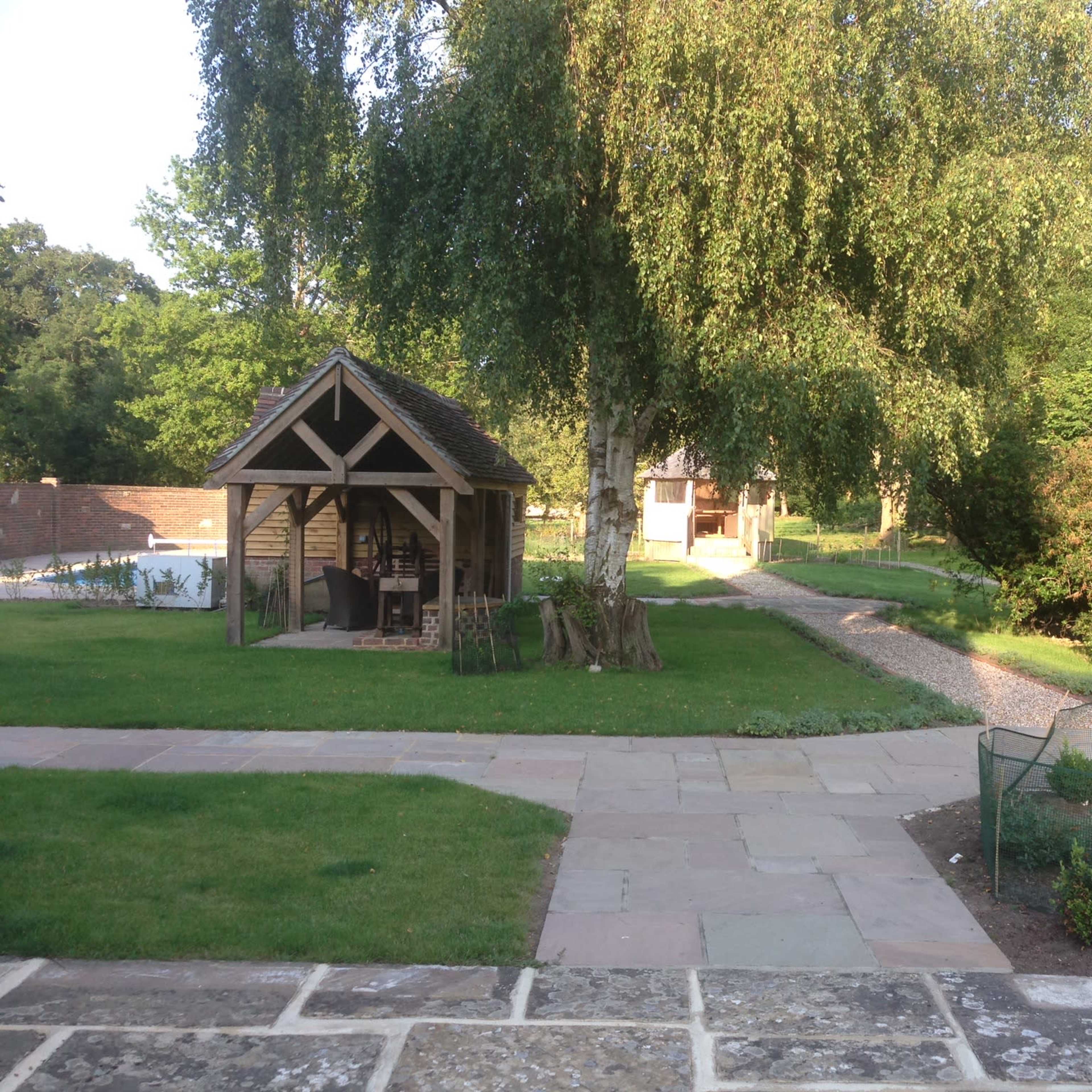 A garden with a wooden gazebo, a pathway, and lush greenery surrounding the area.