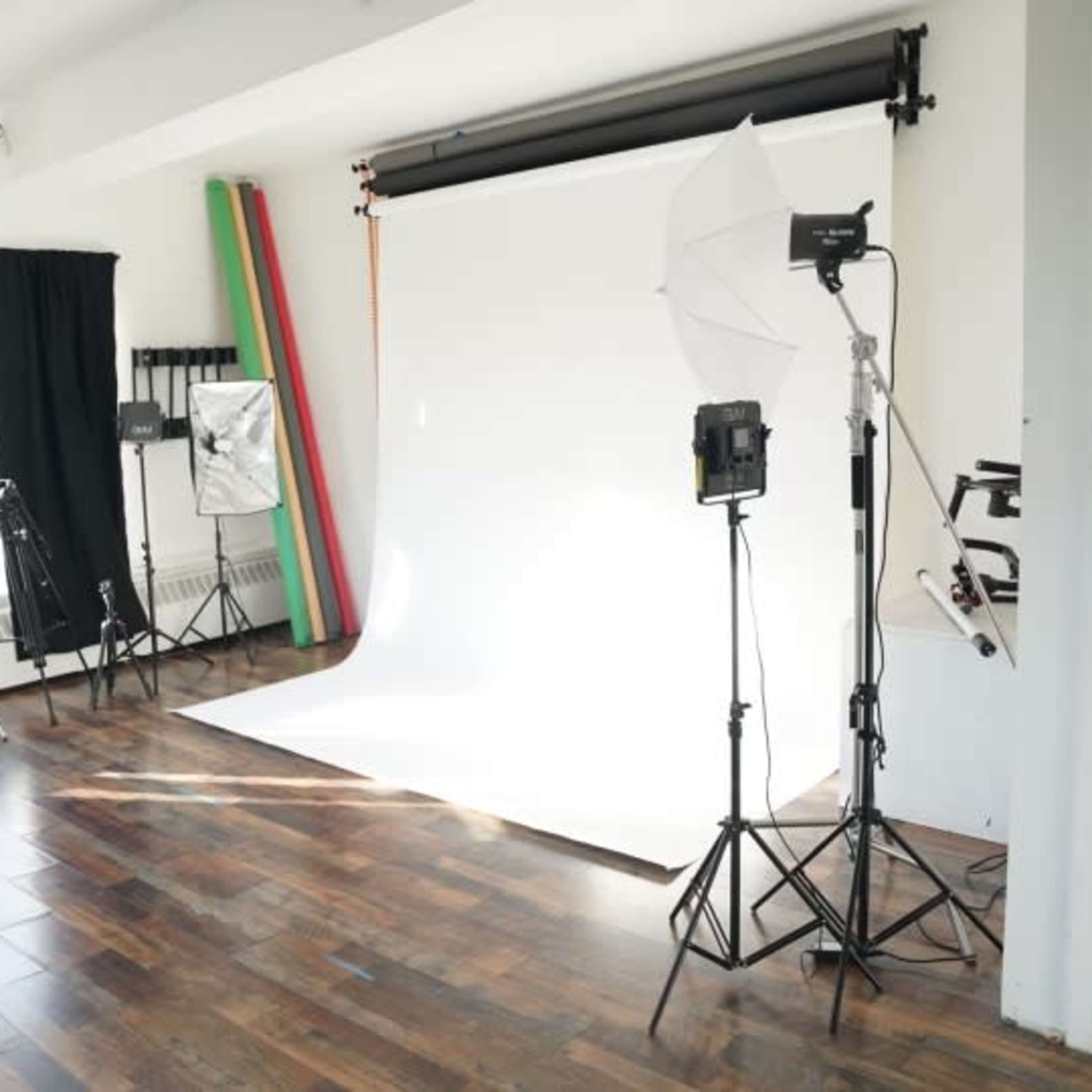 A photography studio with various equipment, including lights, backdrops, and tripods, set up on a hardwood floor.