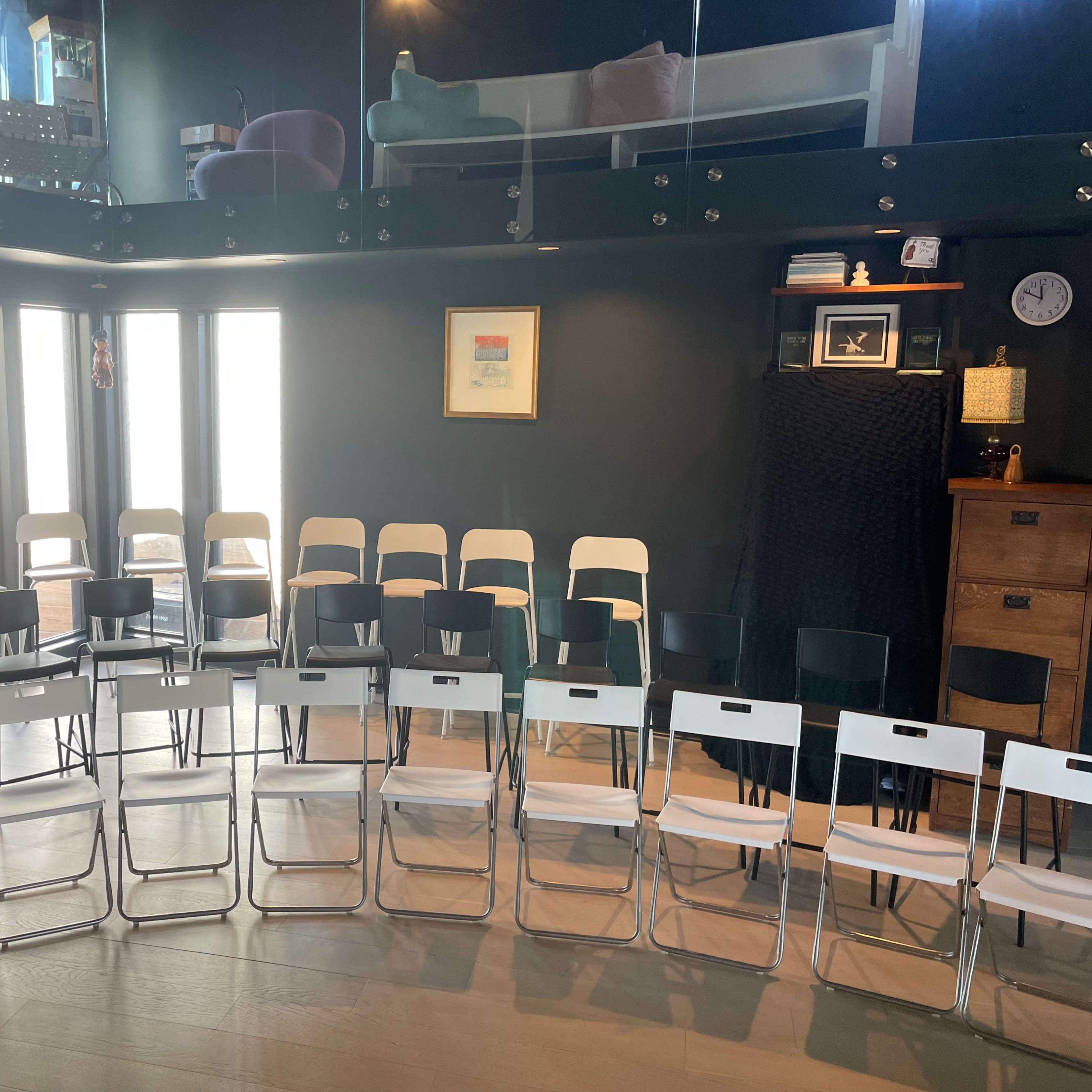 A room arranged with two sets of folding chairs in rows, facing a wall with windows and a decorative piece.
