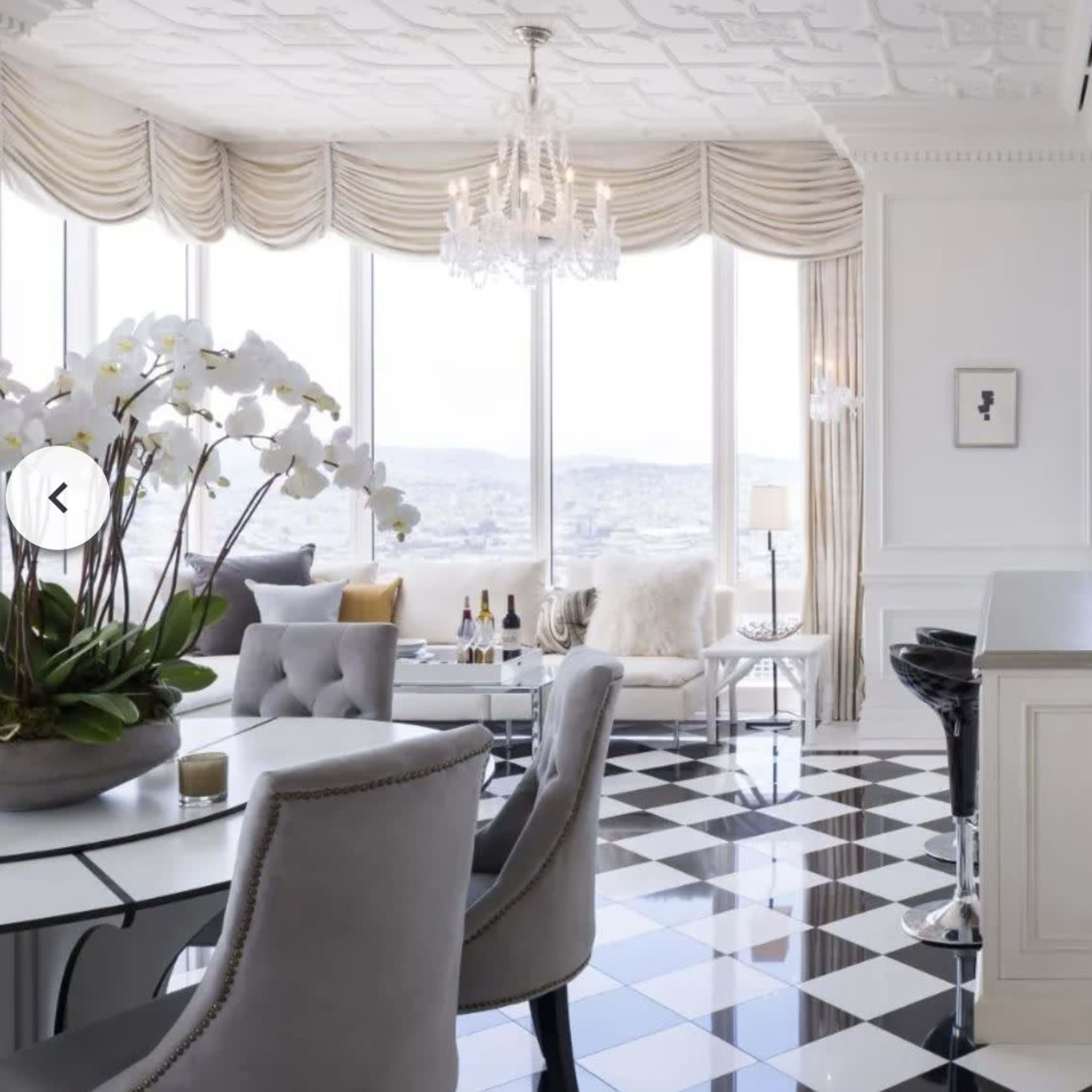 A modern kitchen and dining area with large windows offering a city view, featuring a black-and-white checkered floor and elegant furnishings.