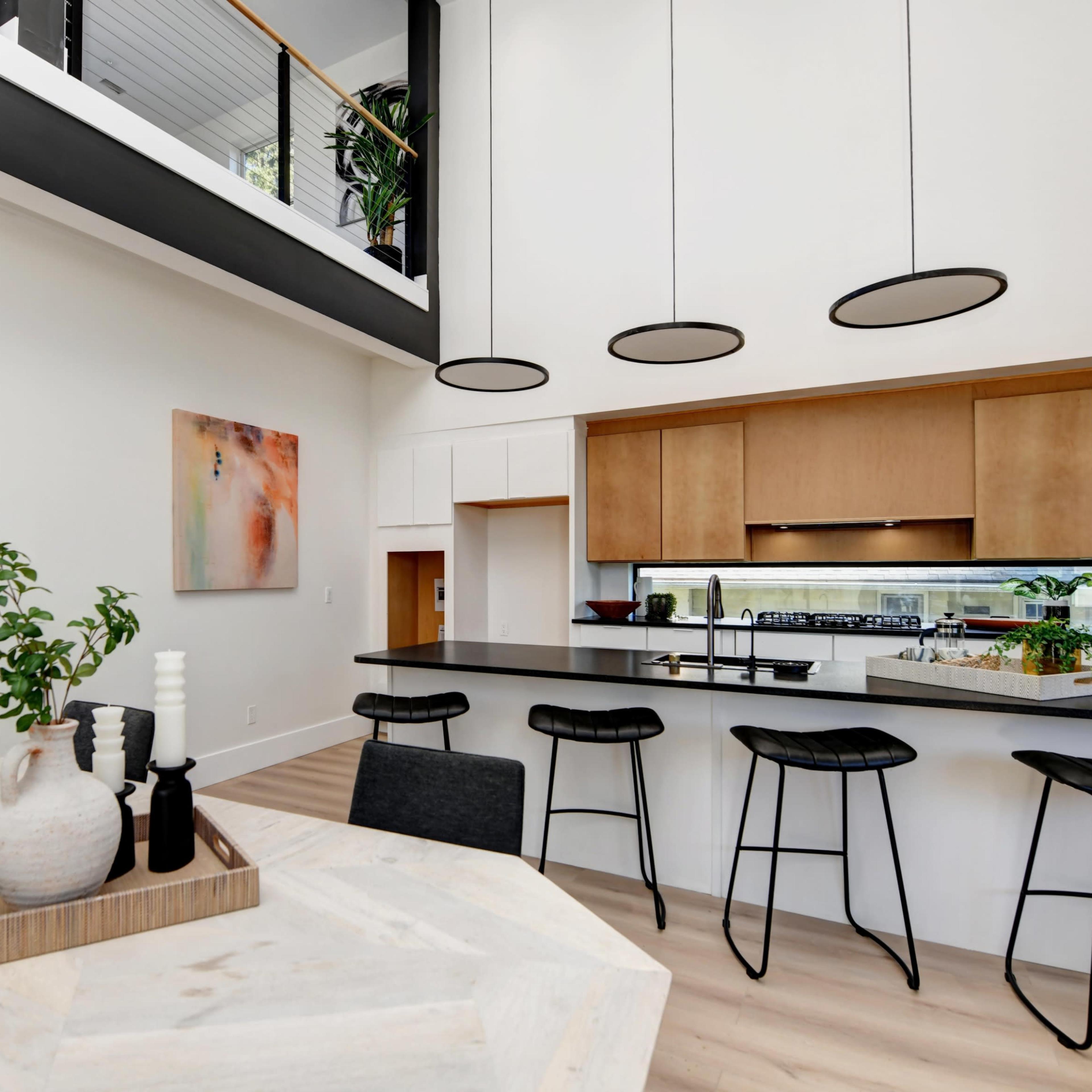 A modern kitchen features a sleek island with bar stools, surrounded by light-colored wood cabinetry and large windows.