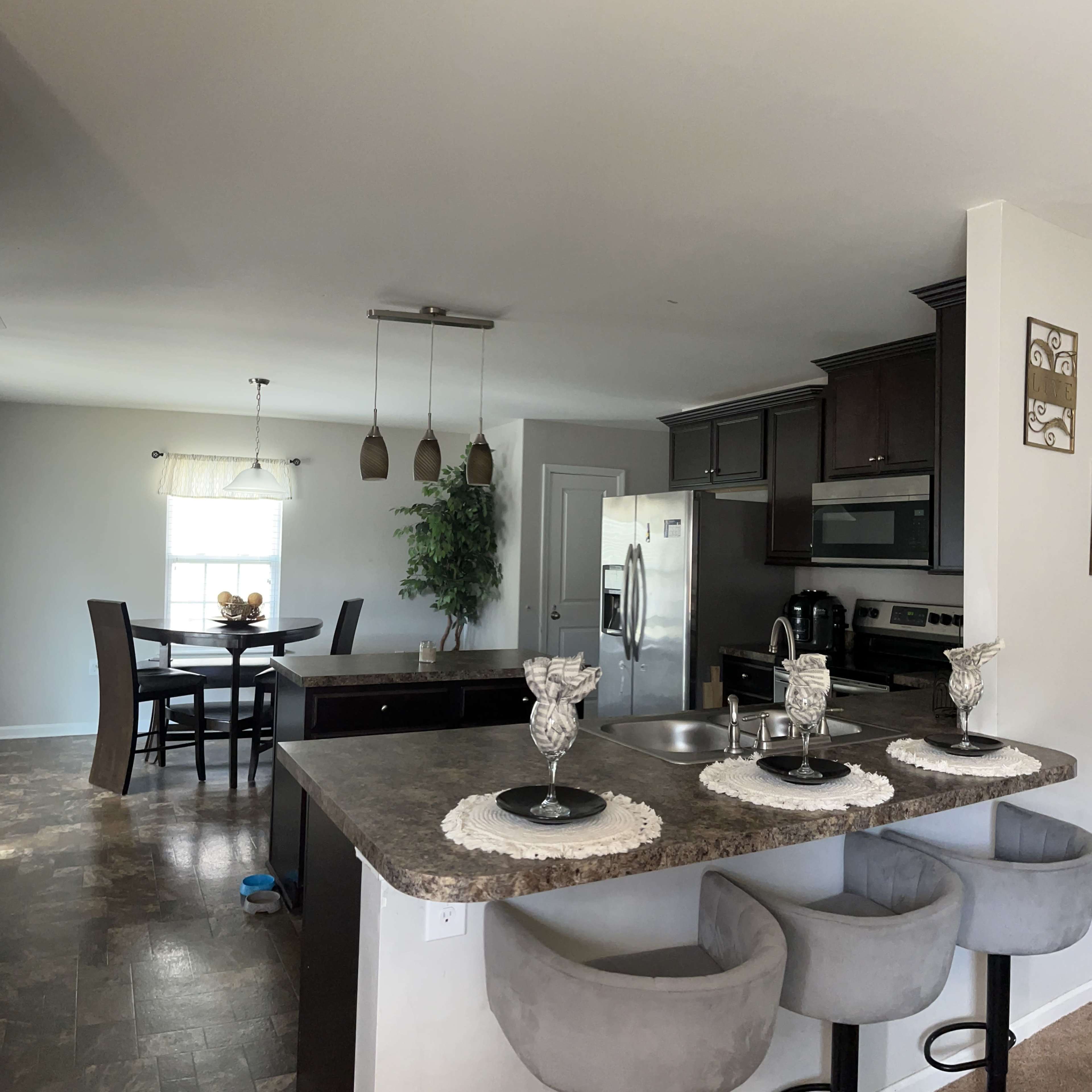 A modern kitchen with a central island, bar stools, and a dining area featuring a table and chairs, all set in a light-colored room.