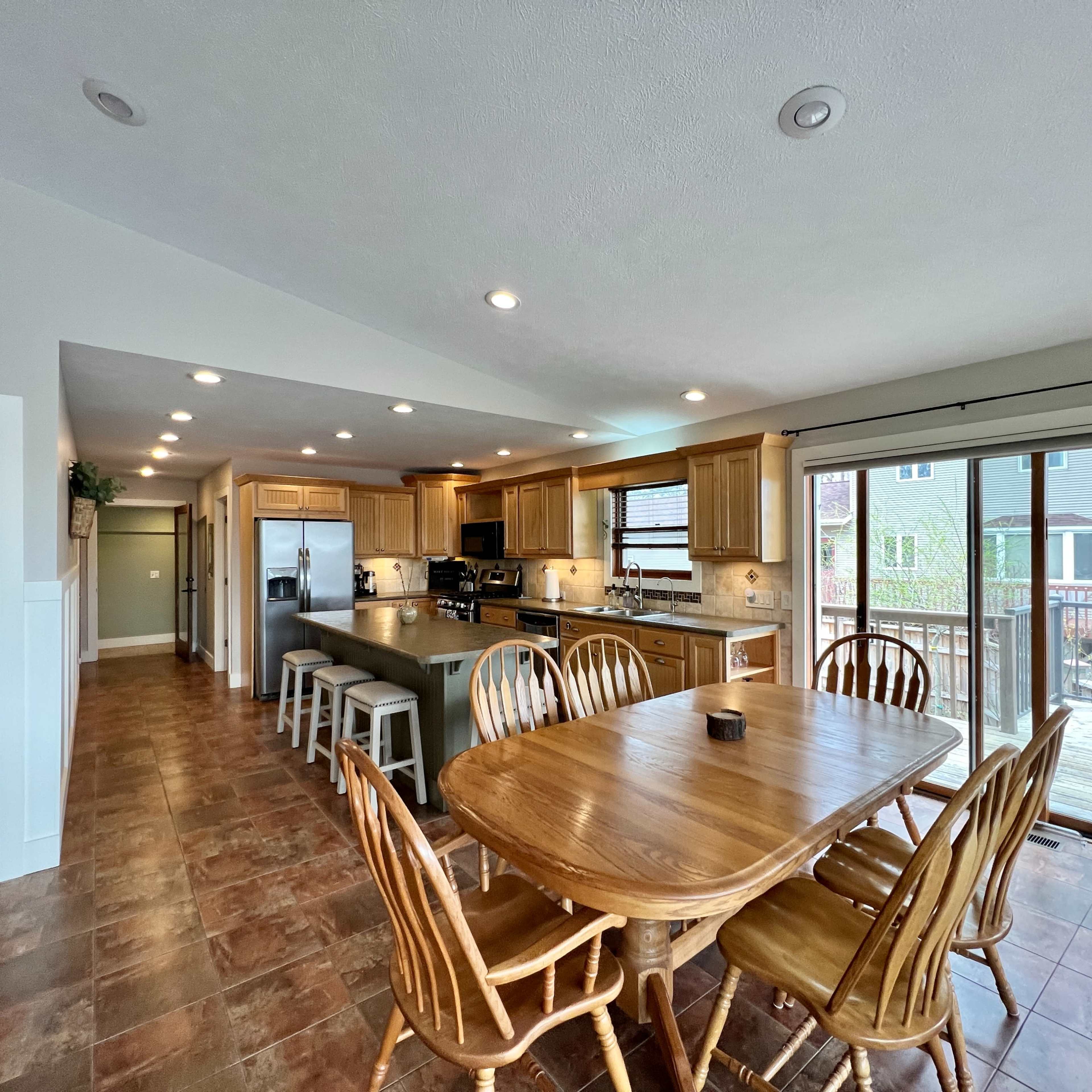 A spacious kitchen and dining area features wooden cabinets, a large island, and a sliding glass door leading to an outdoor deck.