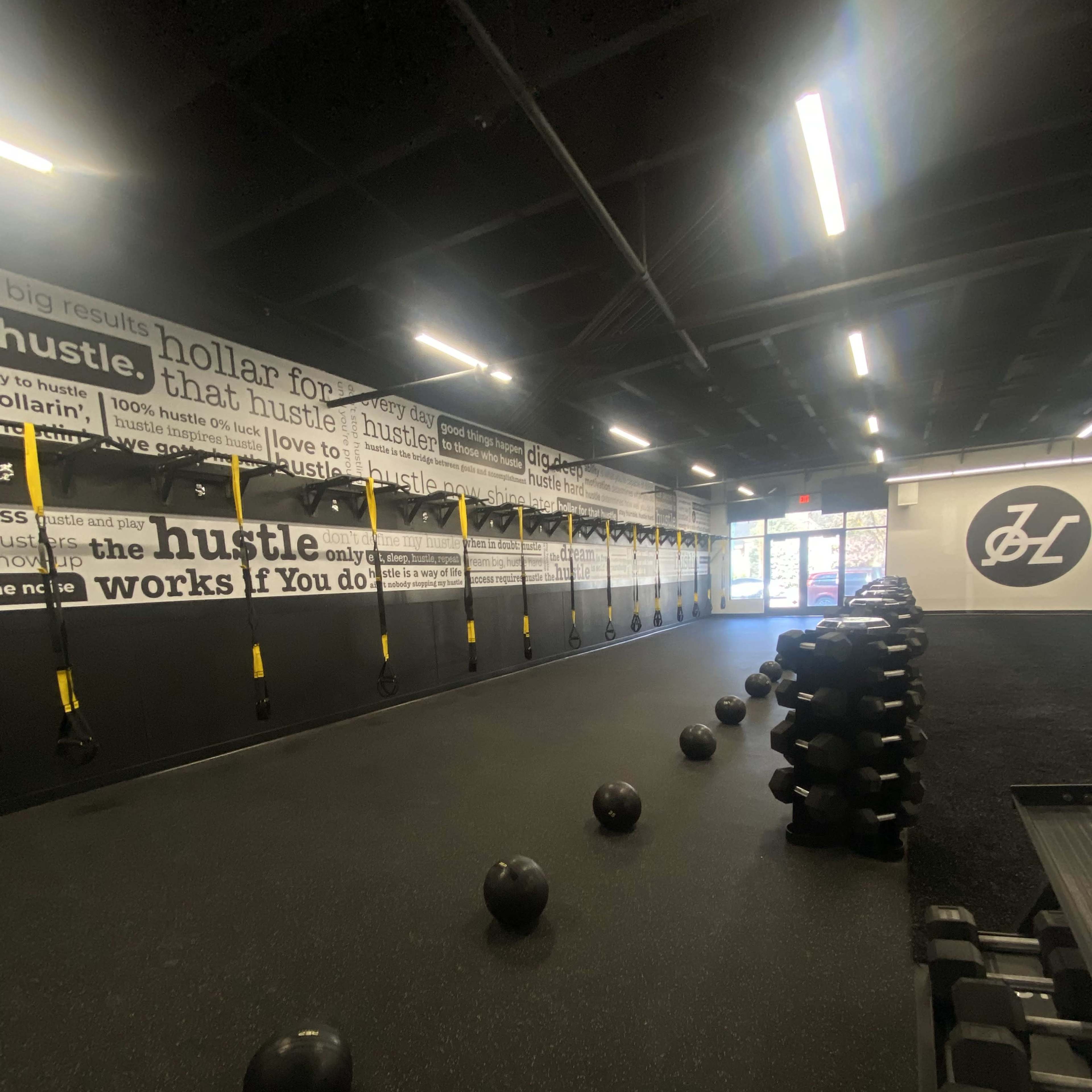 A fitness studio with medicine balls and dumbbells arranged on the floor, and wall-mounted resistance straps along the black walls decorated with motivational phrases.