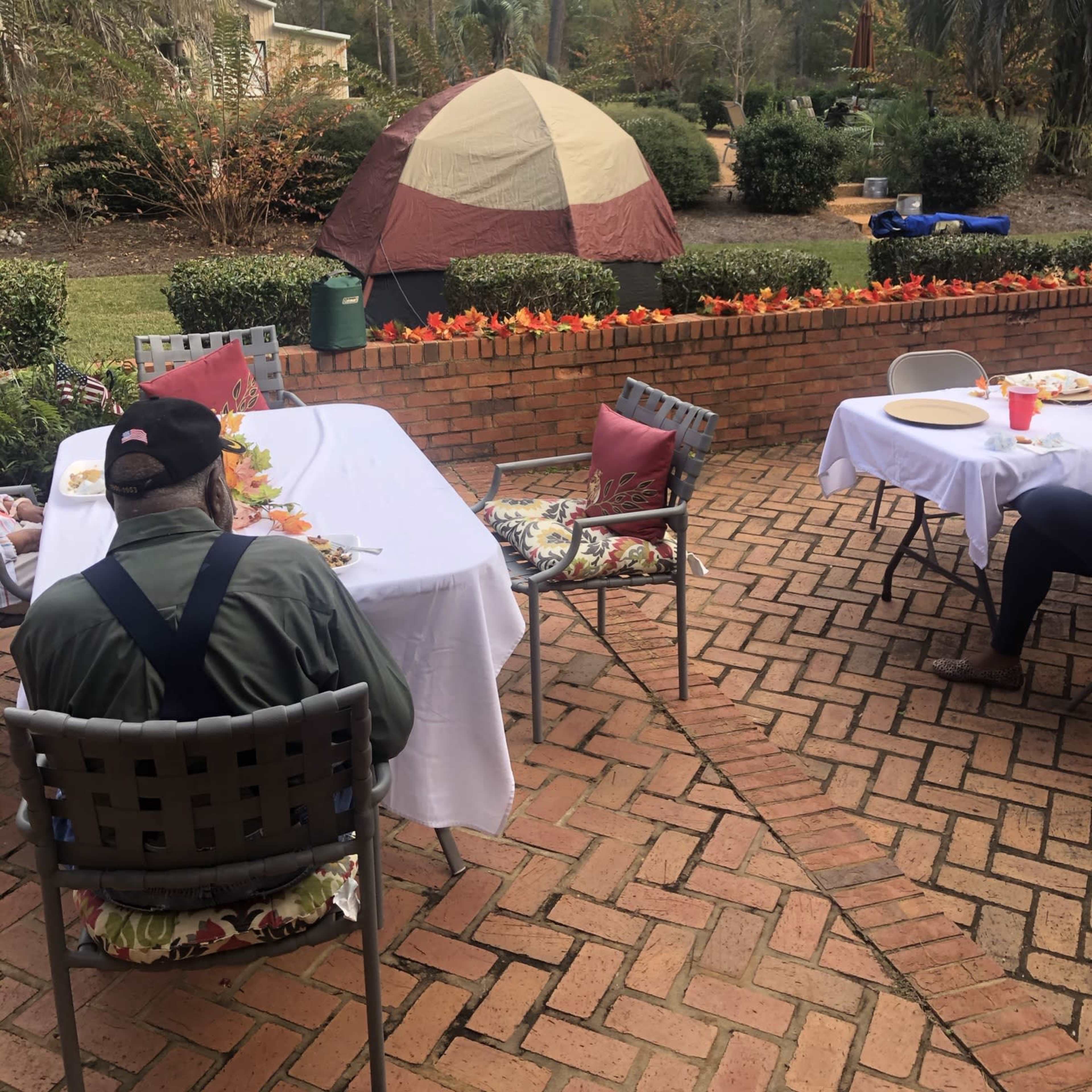 A person sits at a table while a tent is set up in the background of a backyard garden.