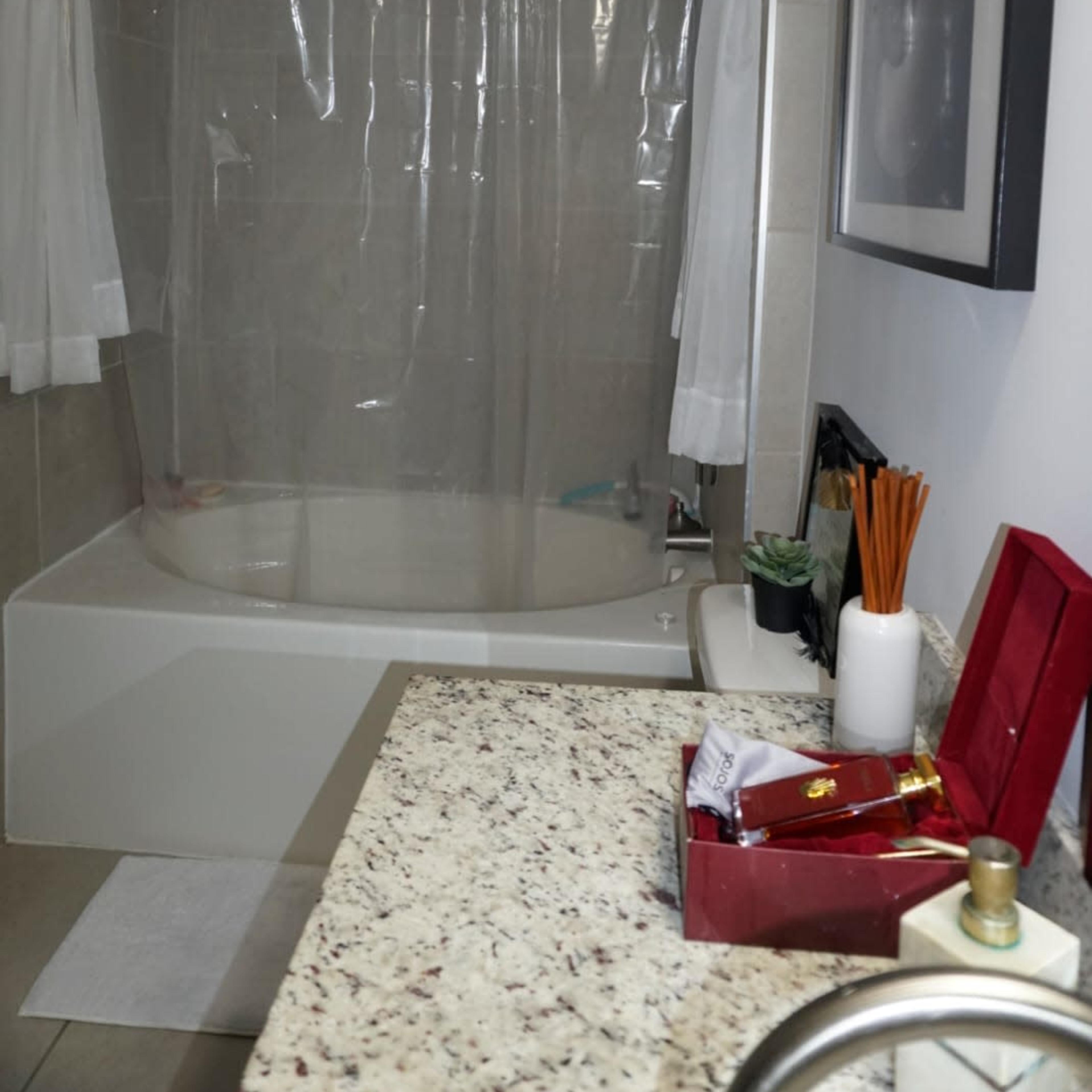 A bathroom with a shower area equipped with a clear plastic curtain, a bathtub, and a countertop featuring decorative items and toiletries.