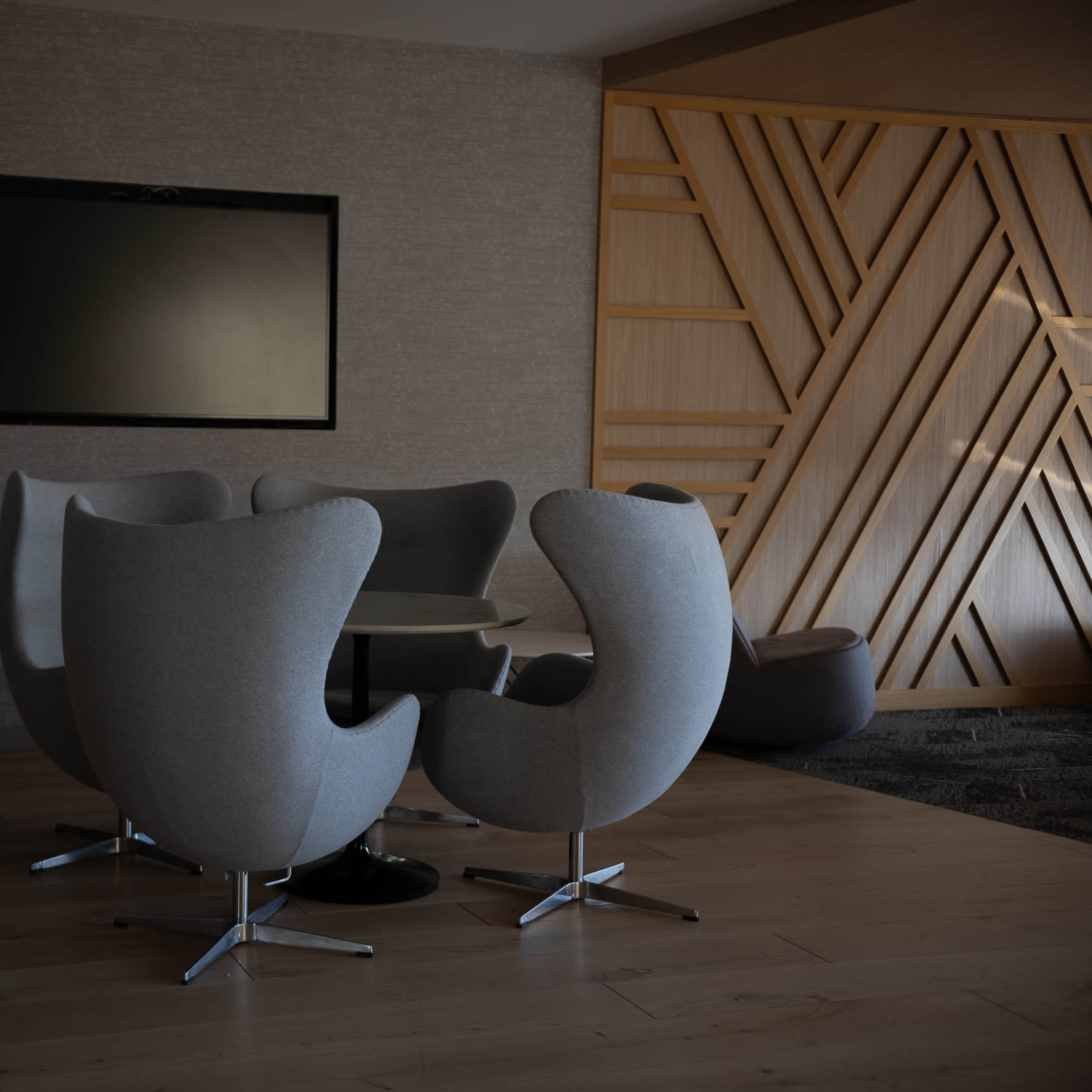 A round table is surrounded by four modern, gray chairs in a well-lit, minimalist lounge area.