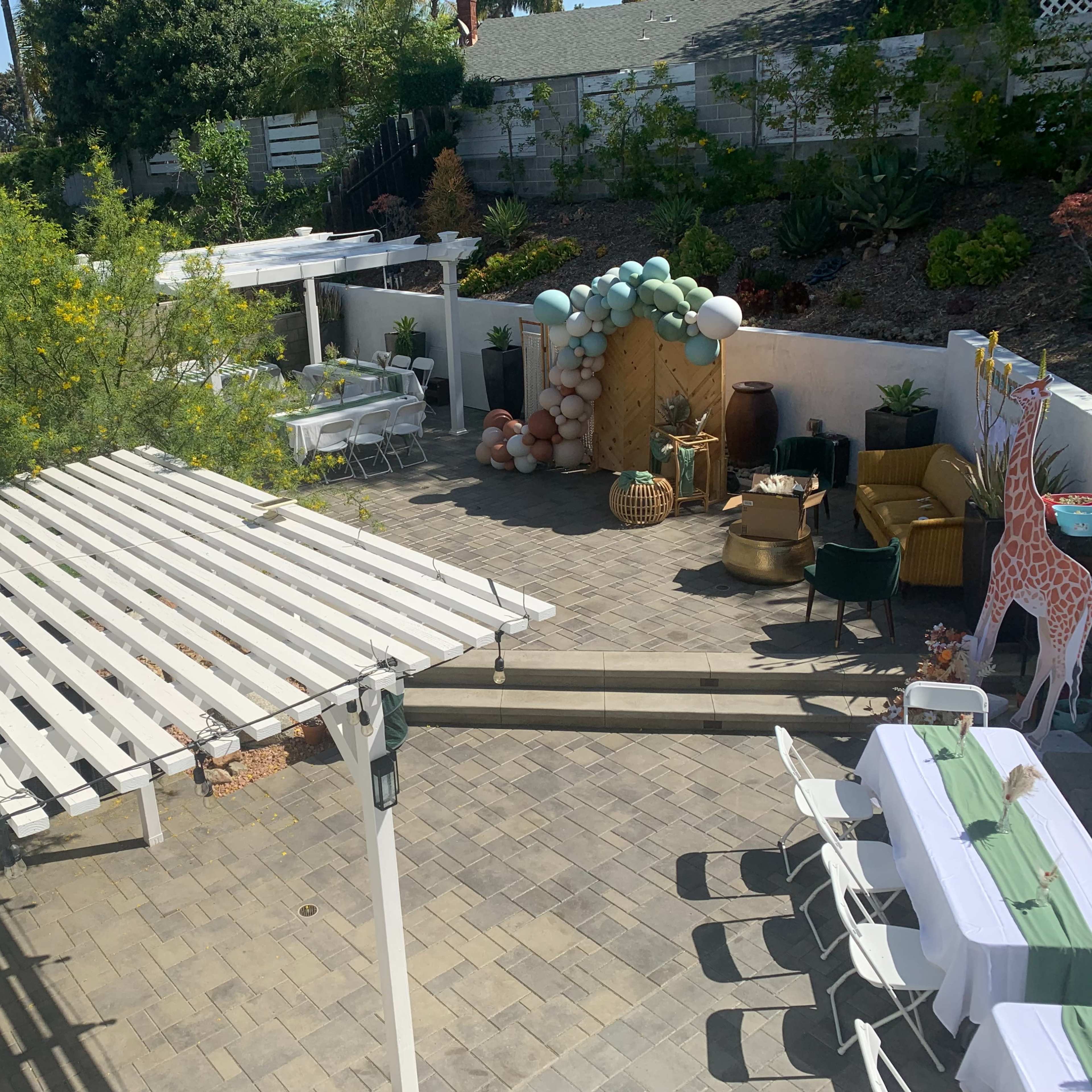 A backyard patio area featuring multiple seating arrangements, a decorative balloon display, and shaded pergolas.
