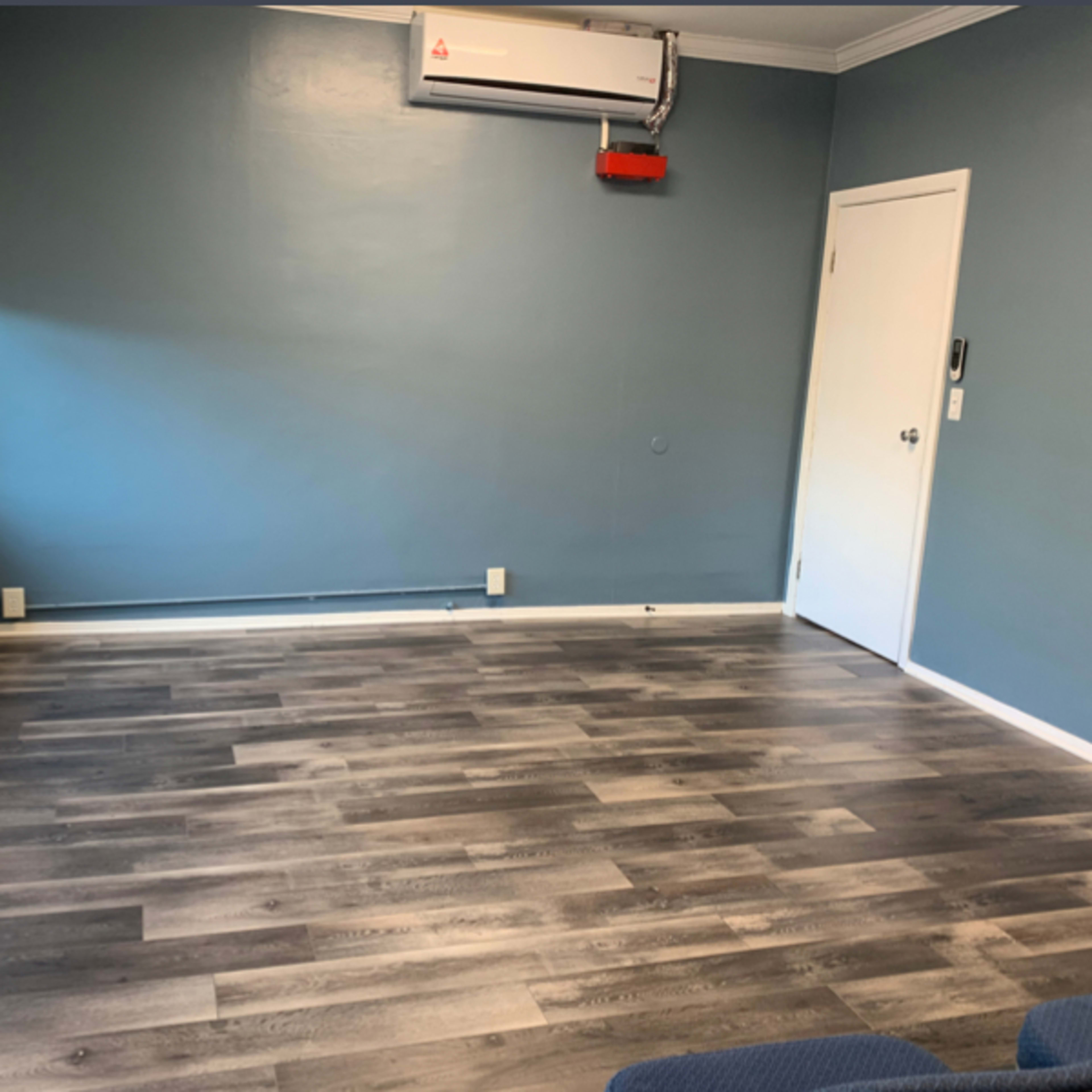 A sparsely furnished room with blue walls, a gray floor, and a door on one side.