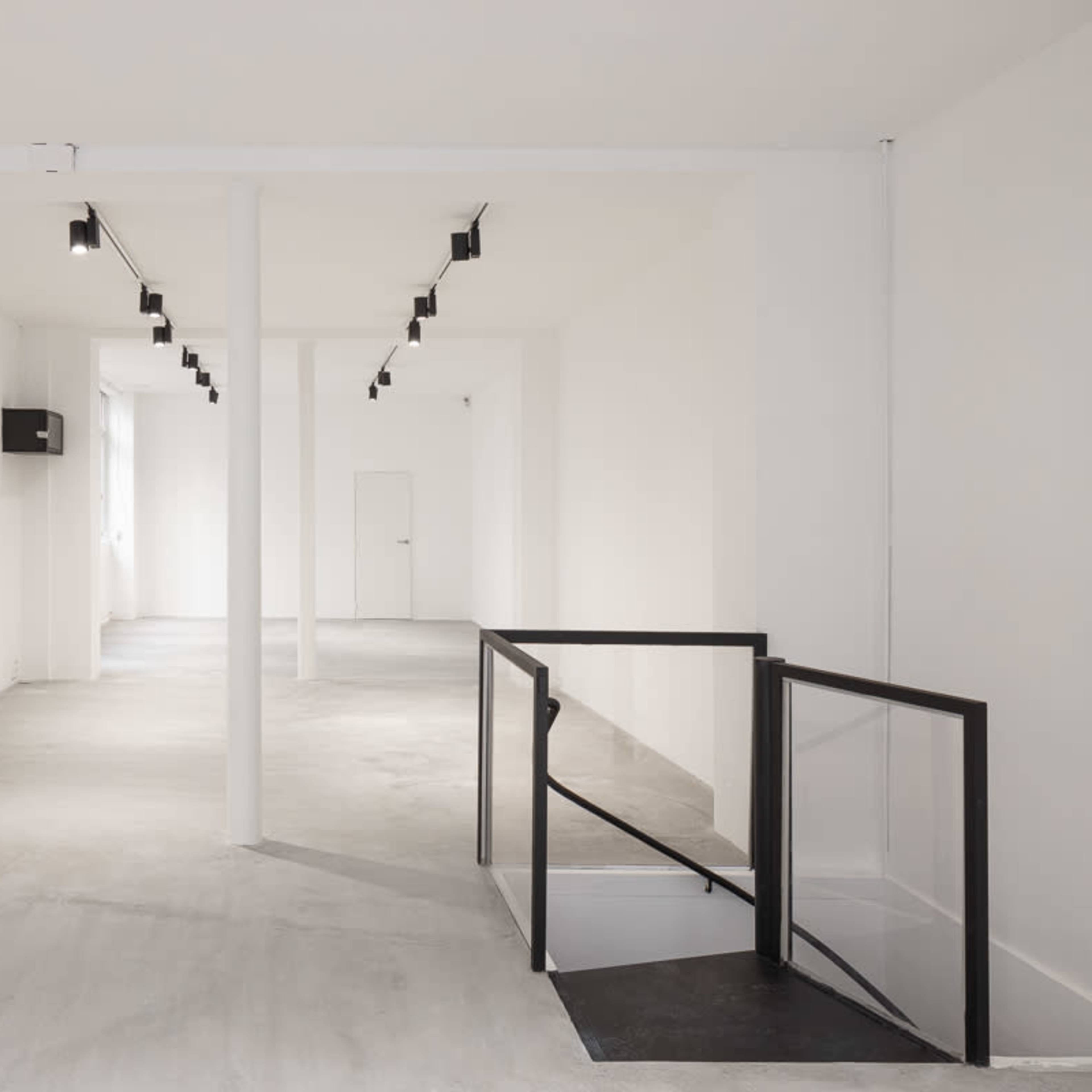 A minimalist, empty room with white walls, concrete flooring, and track lighting along the ceiling.