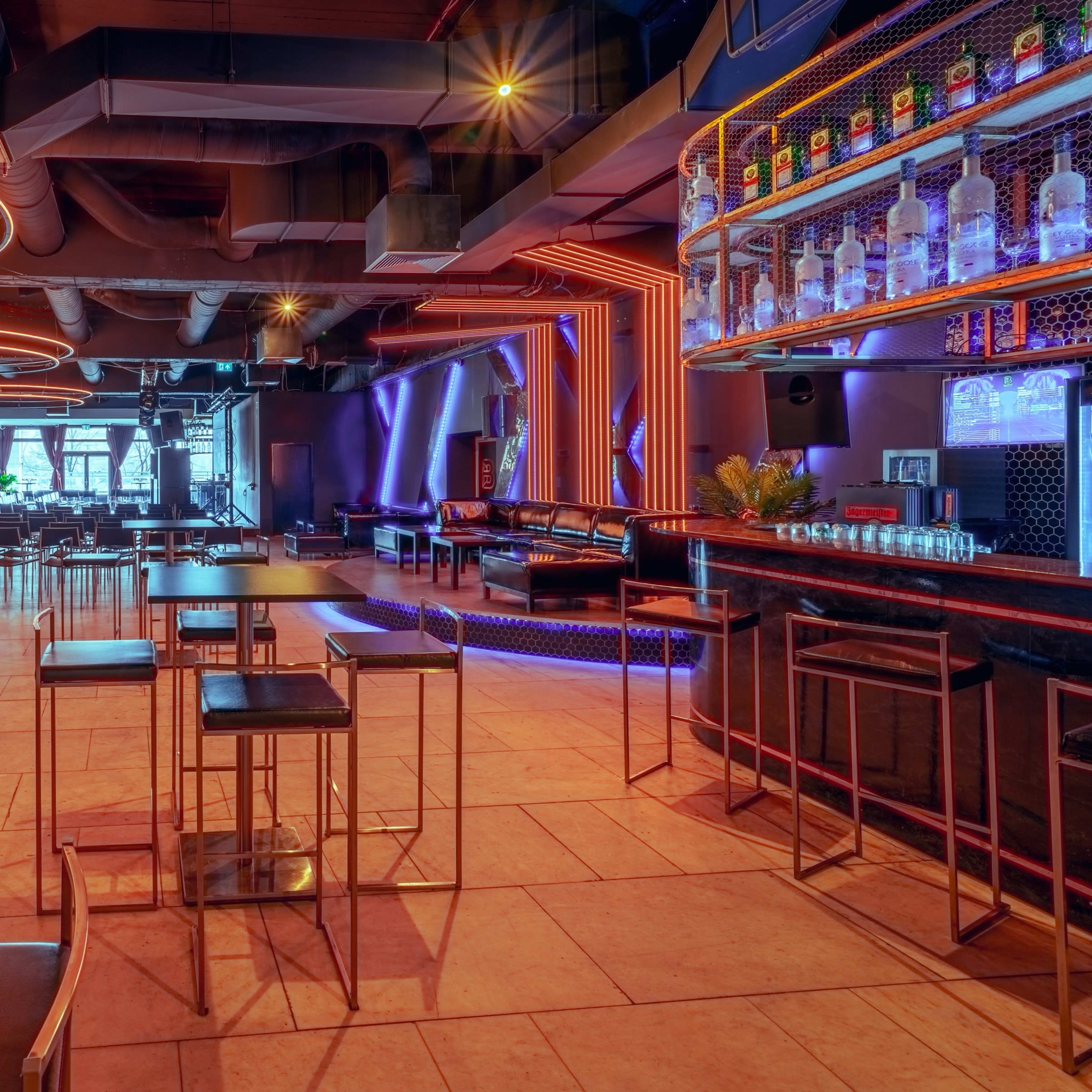 A modern bar interior with illuminated seating areas, a well-stocked bar, and geometric lighting designs.
