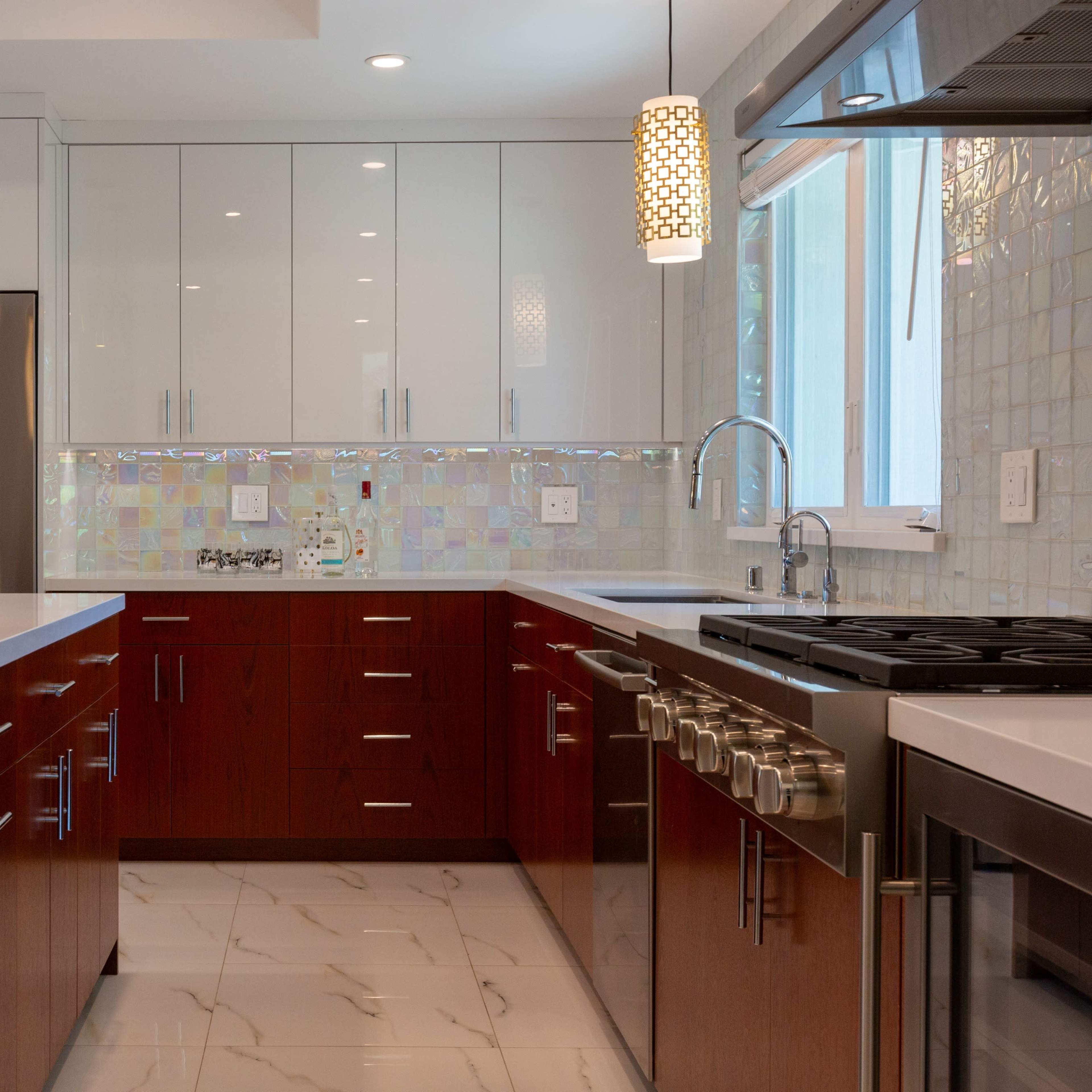 The kitchen features modern cabinetry with a mix of glossy white and warm wood finishes, stainless steel appliances, and a large island with a white countertop.