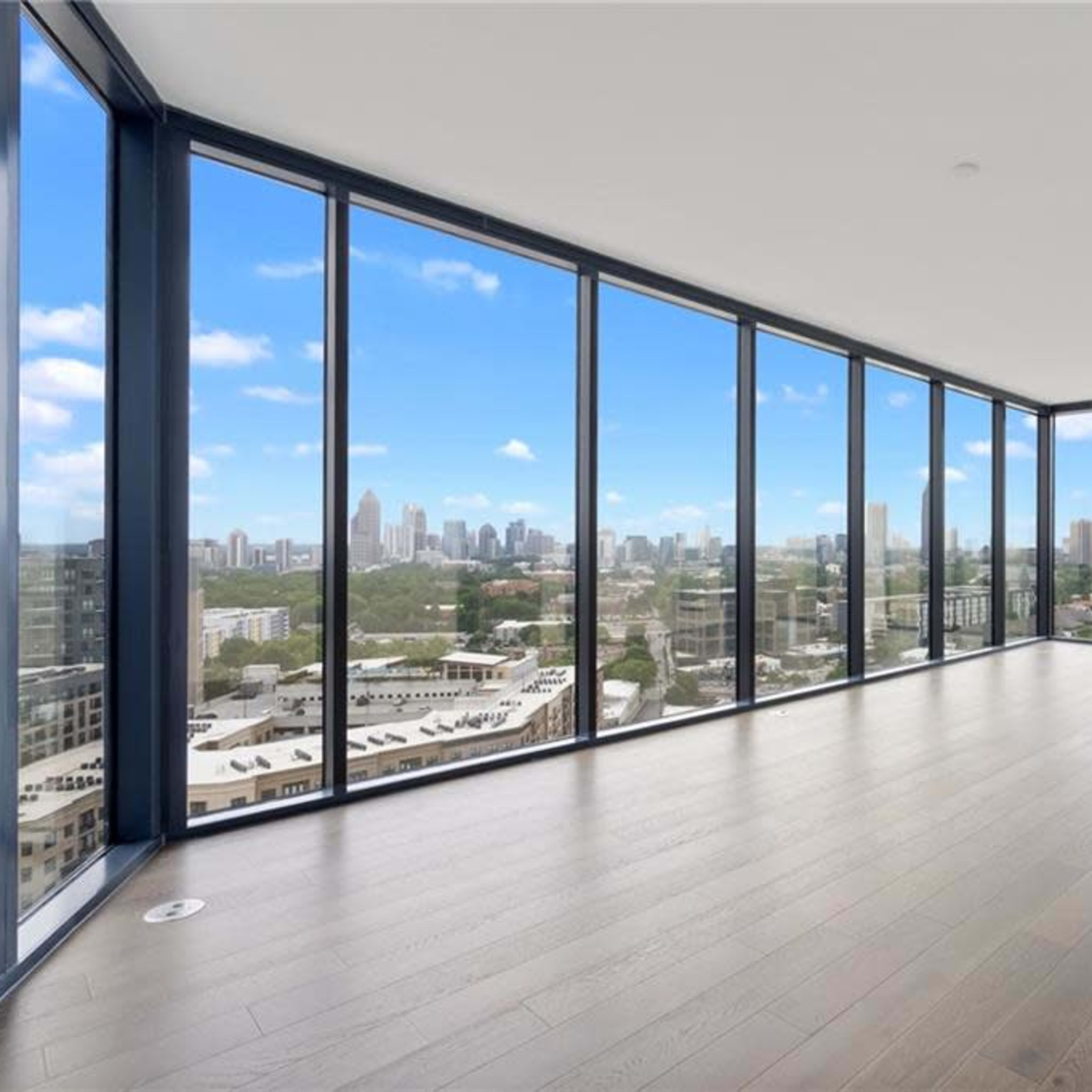 A spacious, empty room with floor-to-ceiling windows offering a view of a city skyline.
