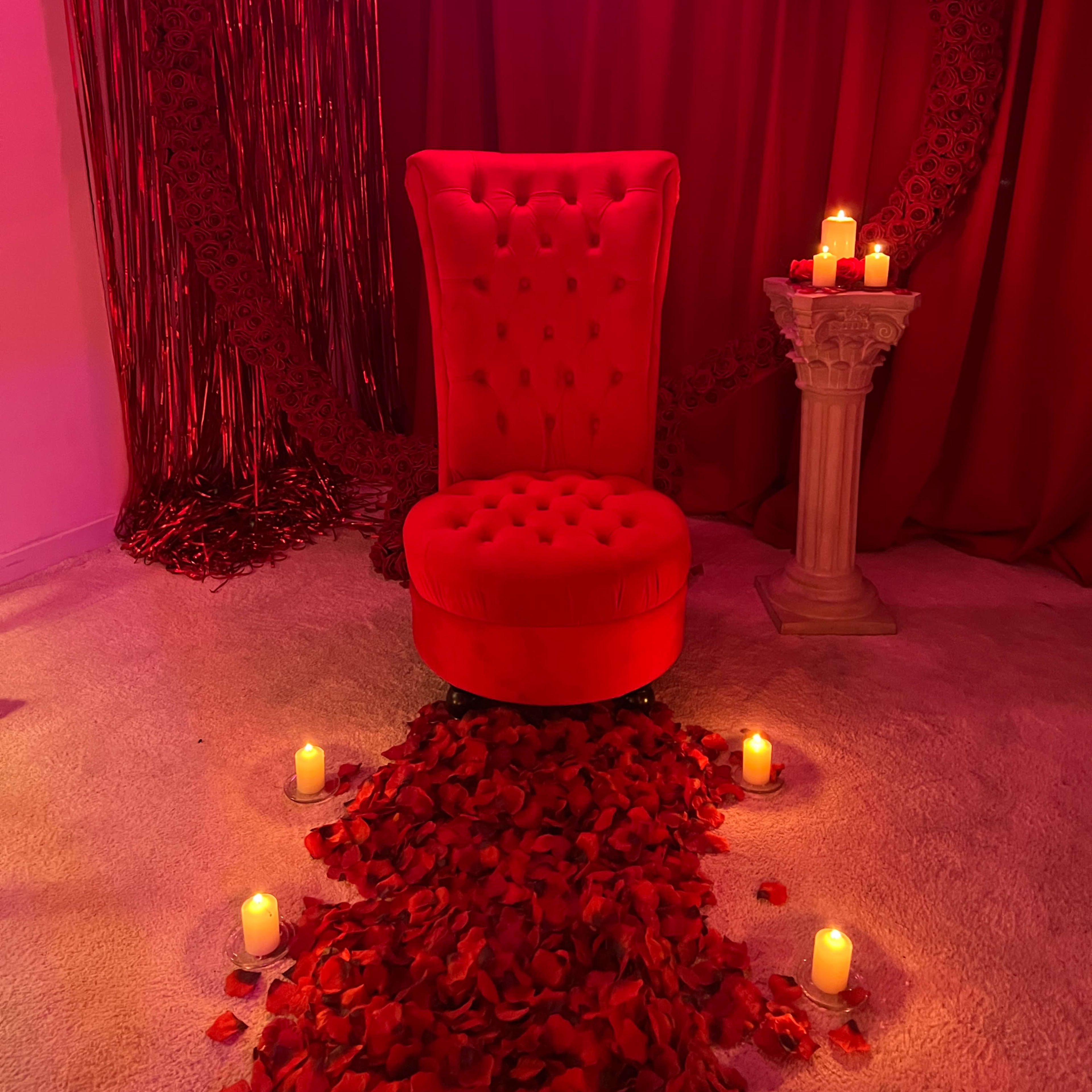A red velvet chair positioned in front of a heart-shaped arrangement of roses and candles, with a neon sign that reads "do what you love."