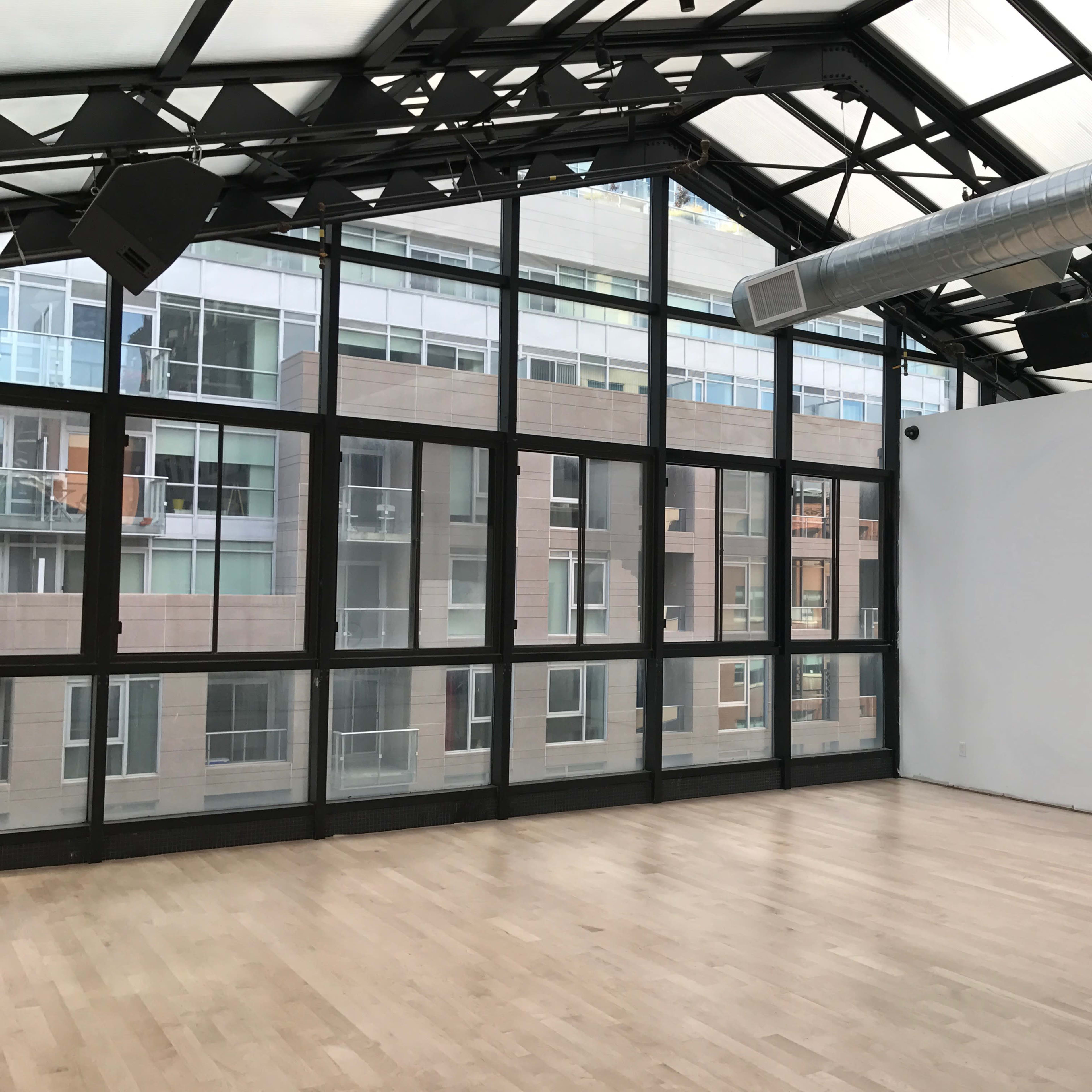 An empty room with wood flooring and large windows showcasing a view of adjacent buildings.