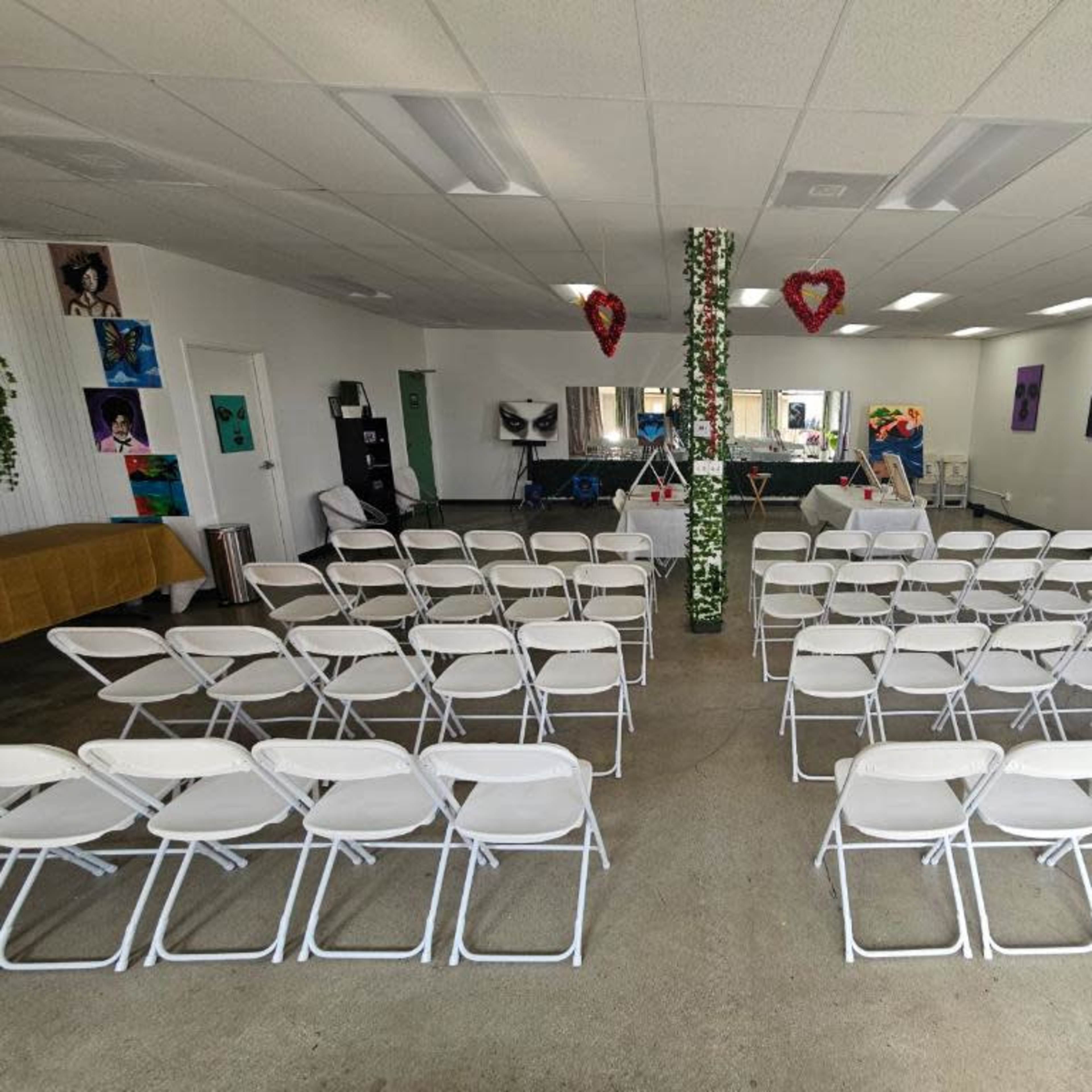 A large room set up with multiple rows of white folding chairs facing a central area adorned with decorations.
