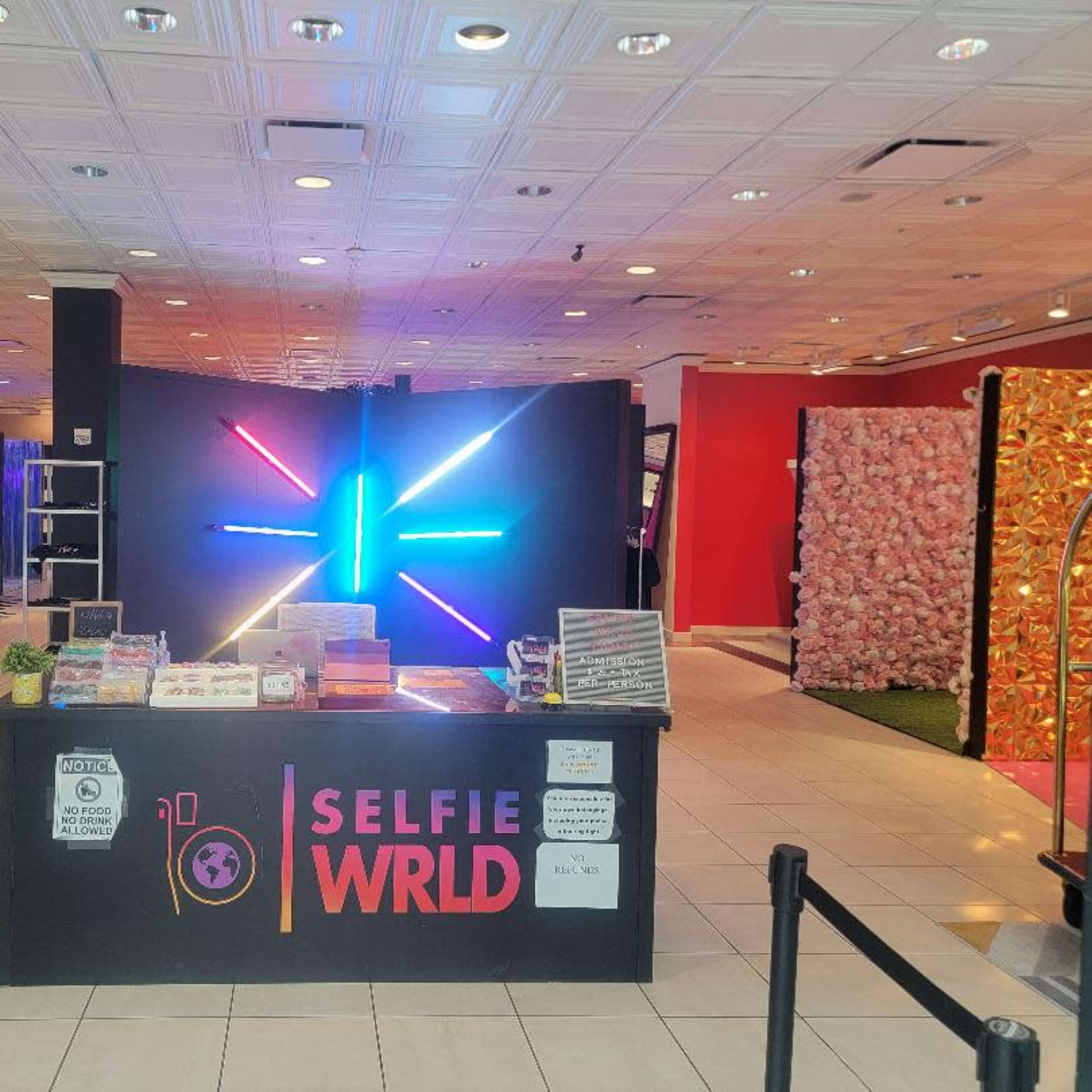 A colorful selfie studio with a central counter labeled "SELFIE WRLD" and vibrant neon lights in the background.