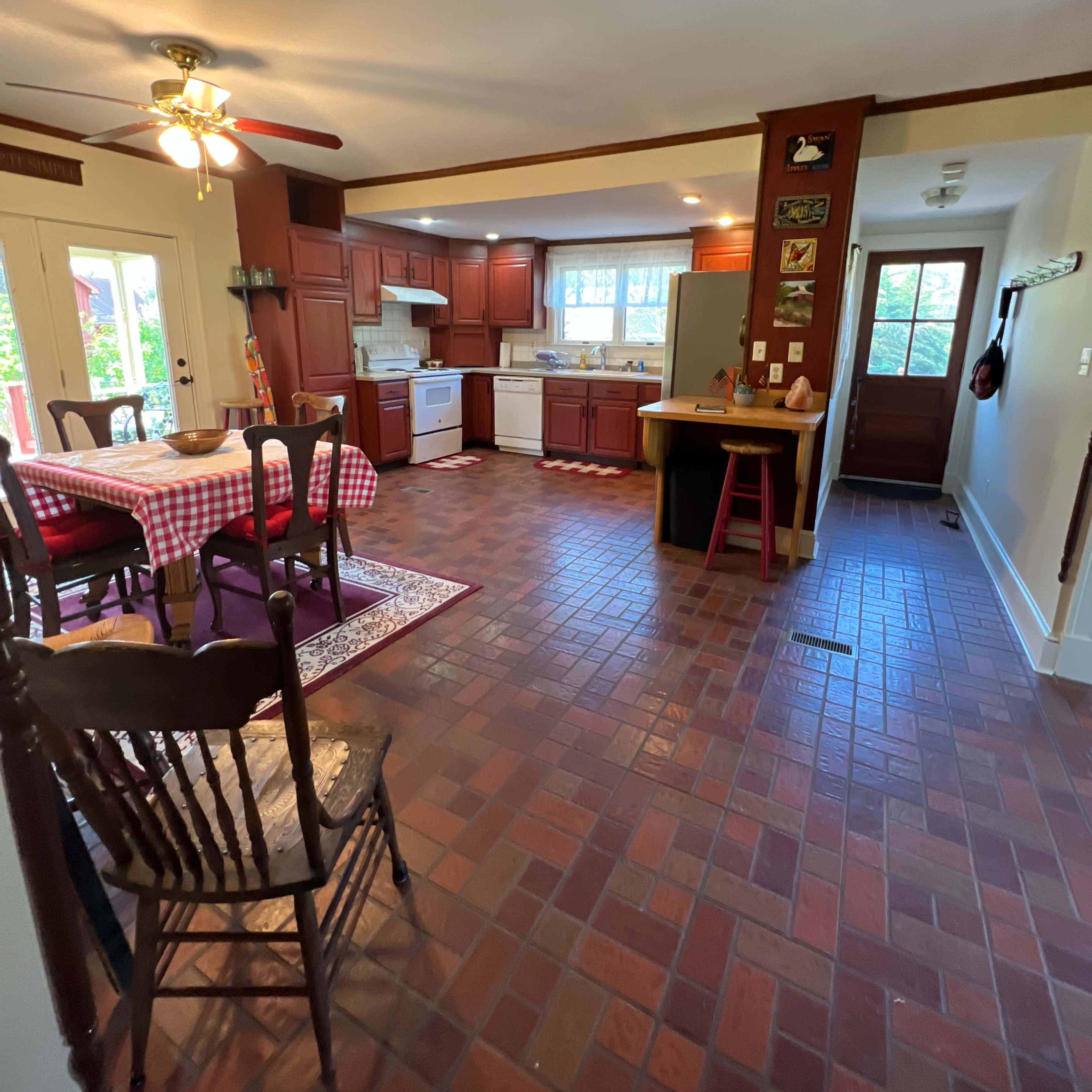 A spacious kitchen features wooden cabinets, a checkered tablecloth on a dining table, and a tile floor.