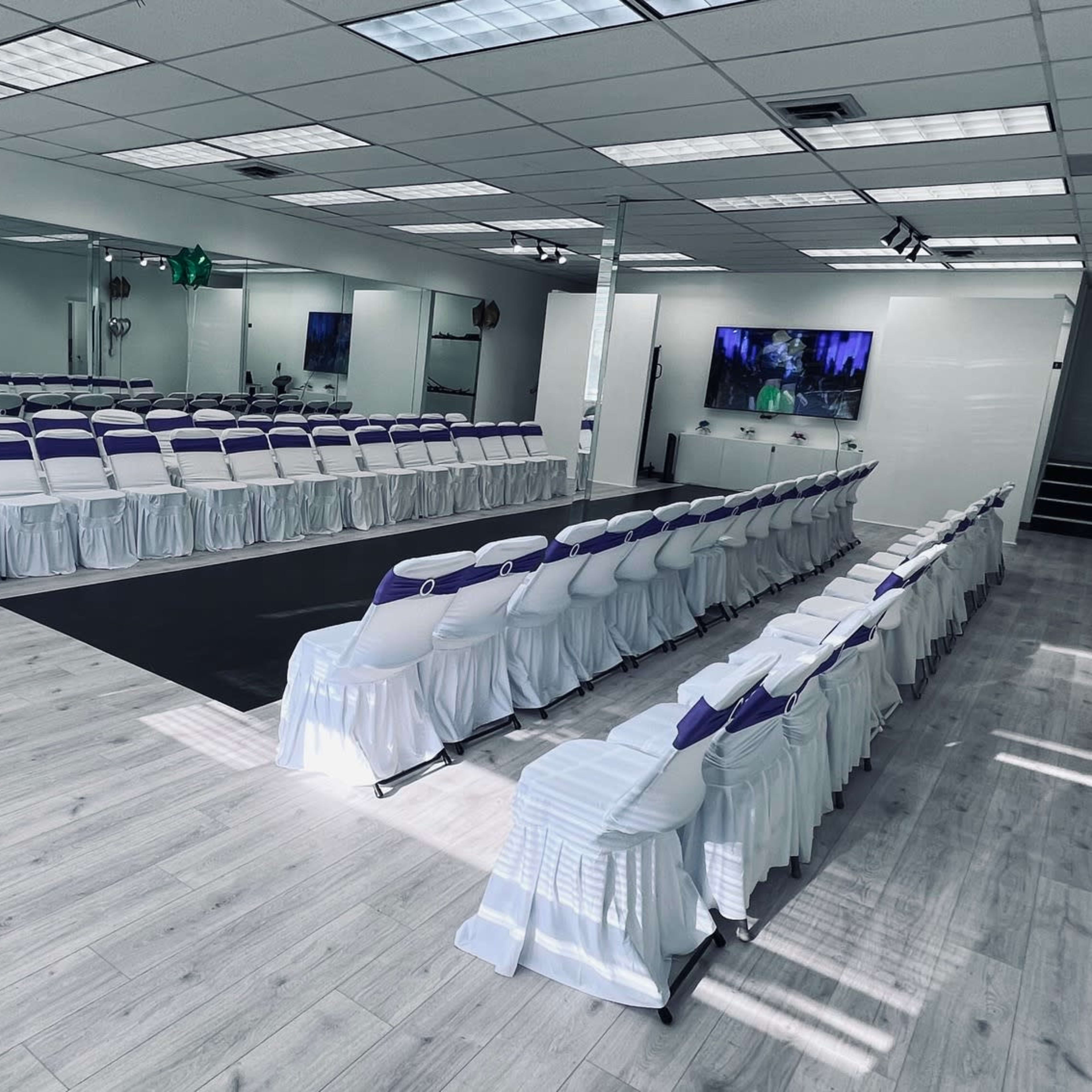 A well-arranged indoor event space with rows of chairs covered in white and purple, set up for a gathering.
