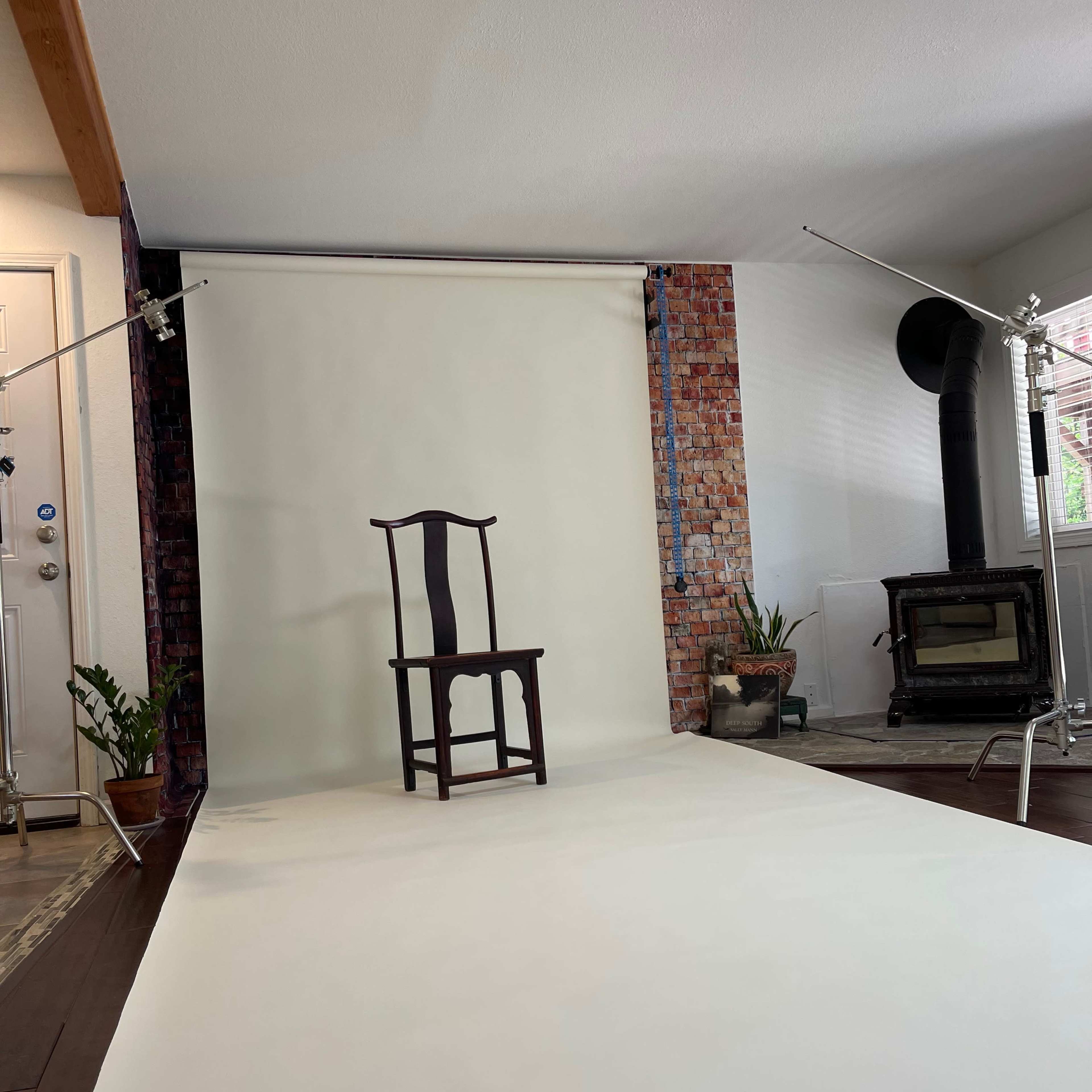 A single wooden chair is centered in a photography studio with a blank backdrop and lighting equipment set up nearby.