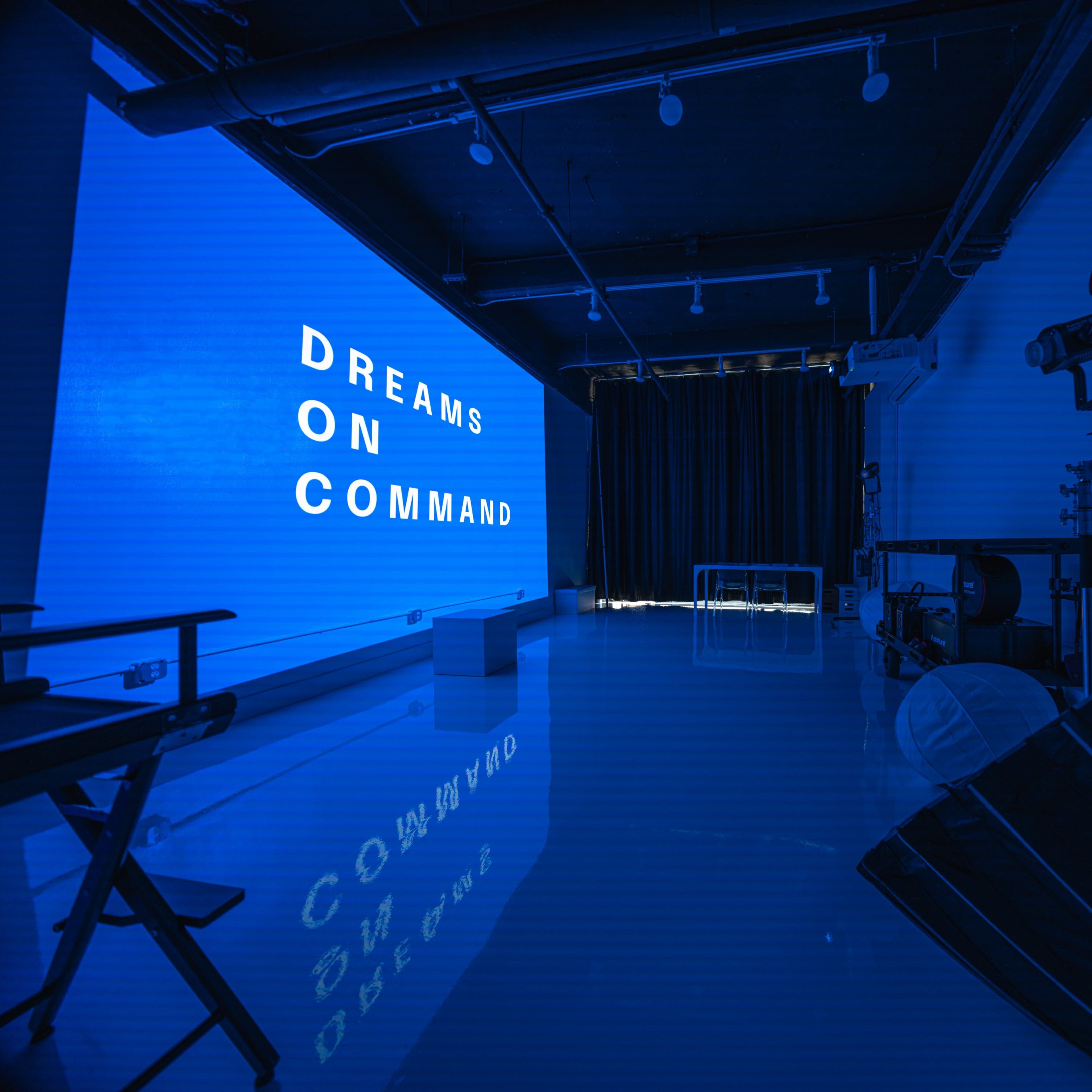 A modern studio space with a blue wall displaying the words "DREAMS ON COMMAND," and various photography equipment arranged in the room.
