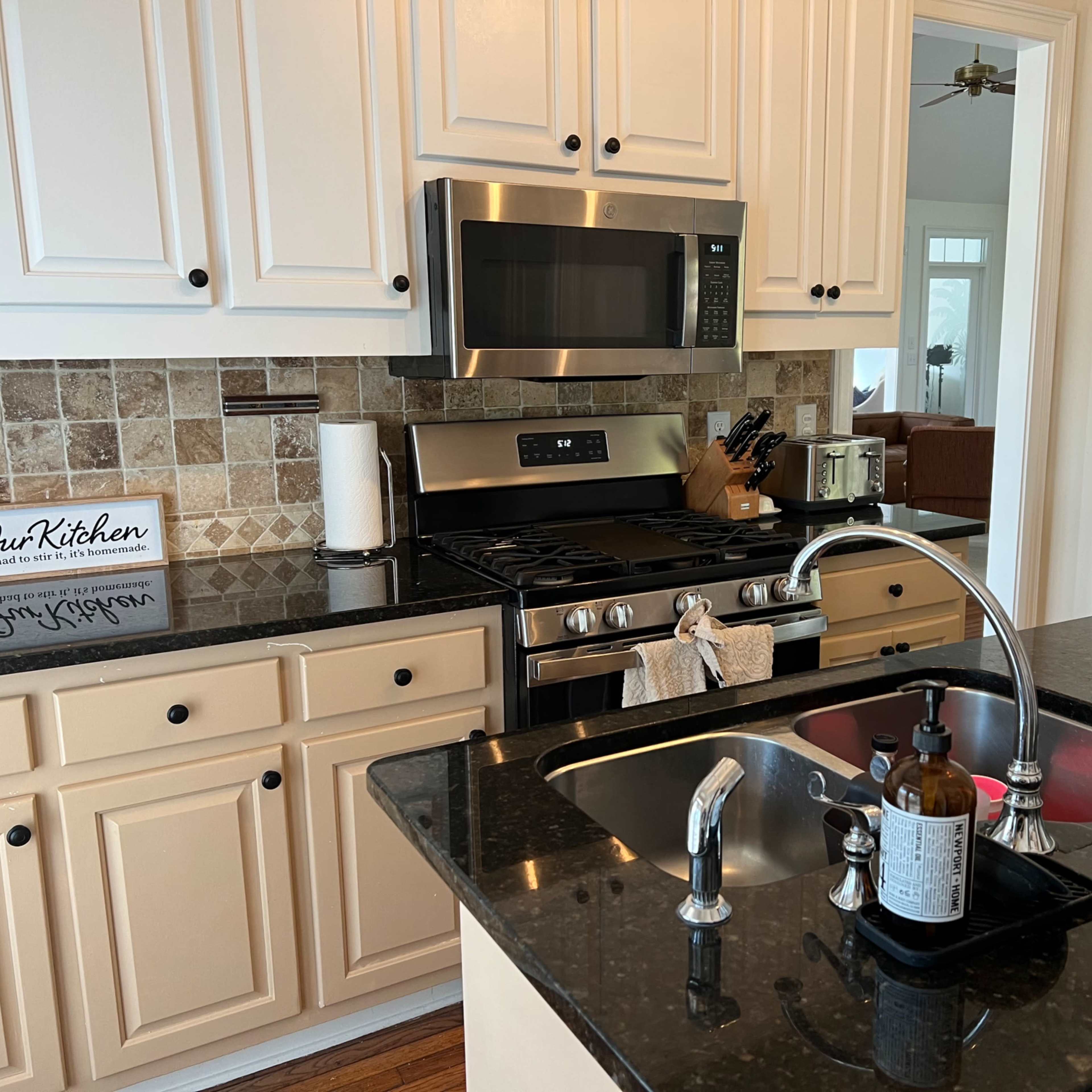 A modern kitchen features stainless steel appliances, dark granite countertops, and light-colored cabinetry with tiled backsplash.