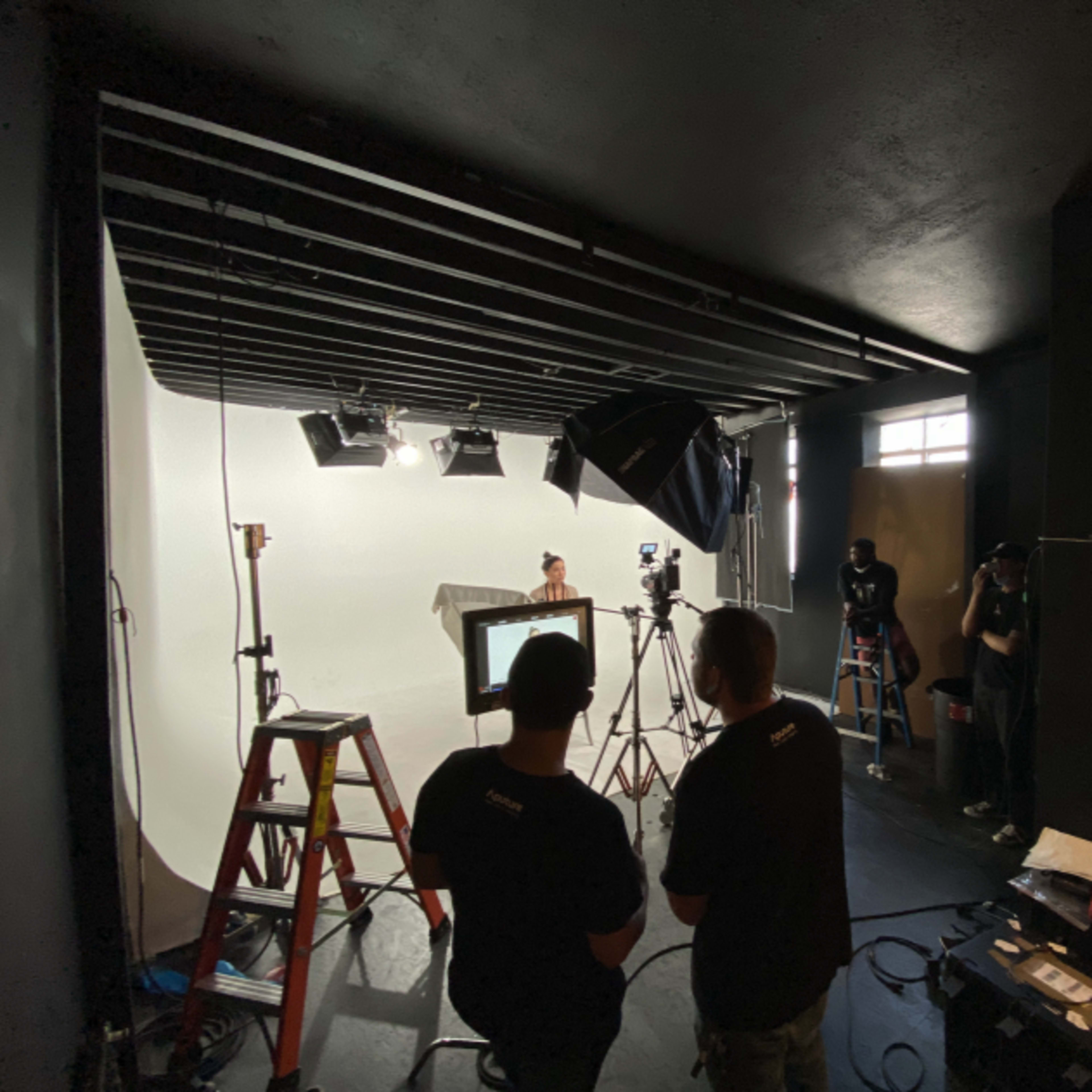 A film set with crew members operating cameras and equipment in a well-lit studio space.