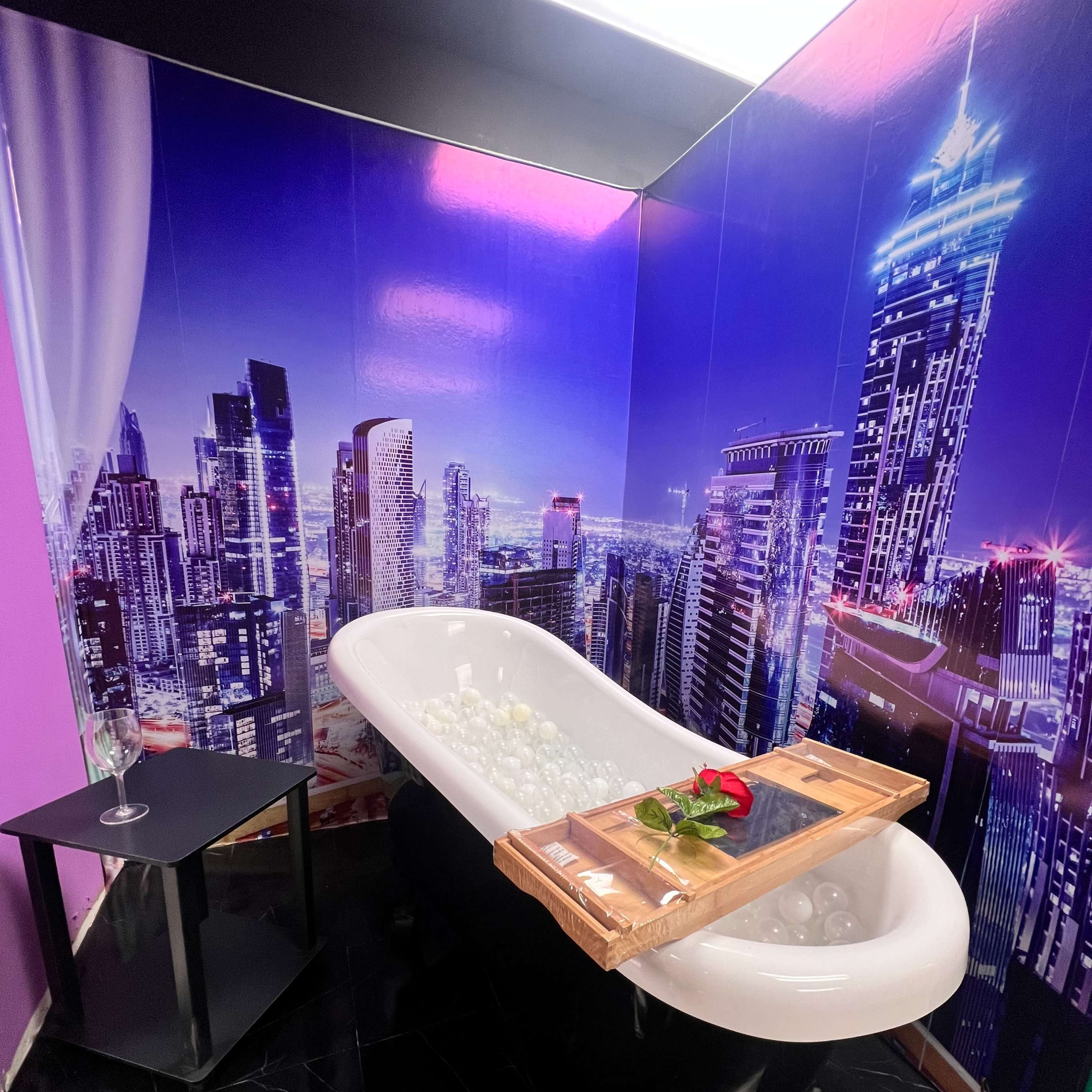 A modern bathtub filled with rose petals and surrounded by a city skyline mural on the wall.