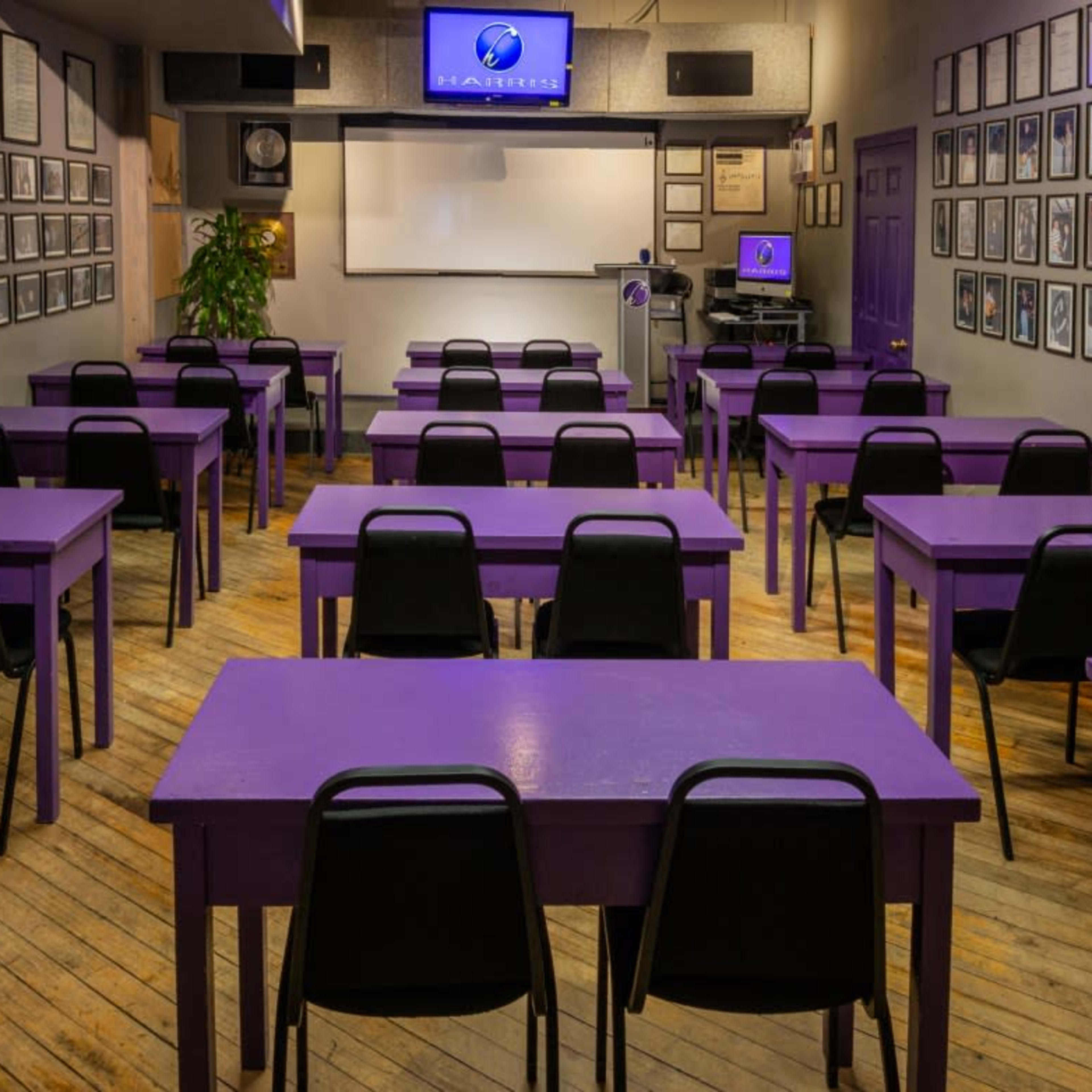 A classroom with purple tables arranged in rows and framed photographs adorning the walls.