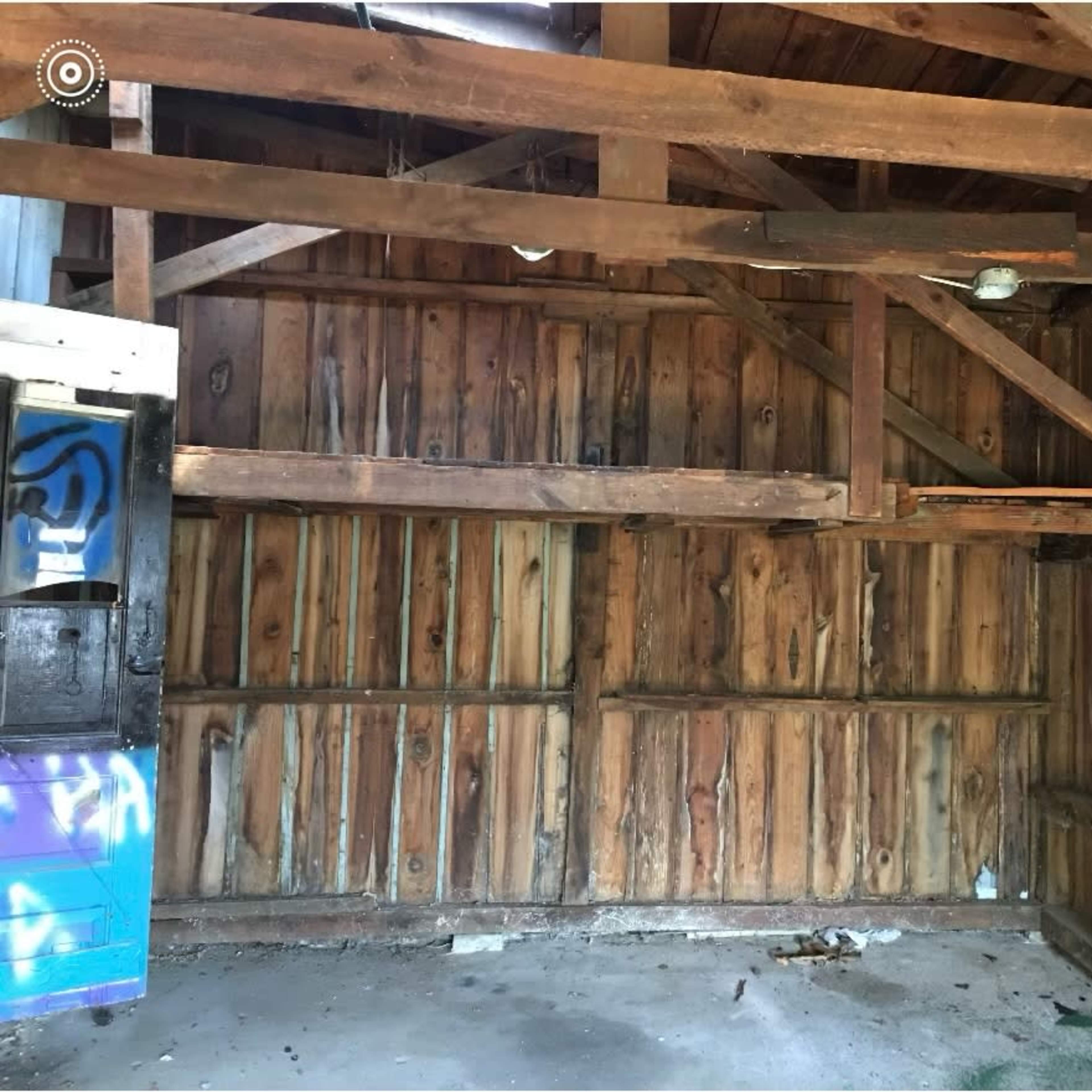 The interior of a wooden structure with exposed beams, featuring unfinished wood walls and a bare floor.