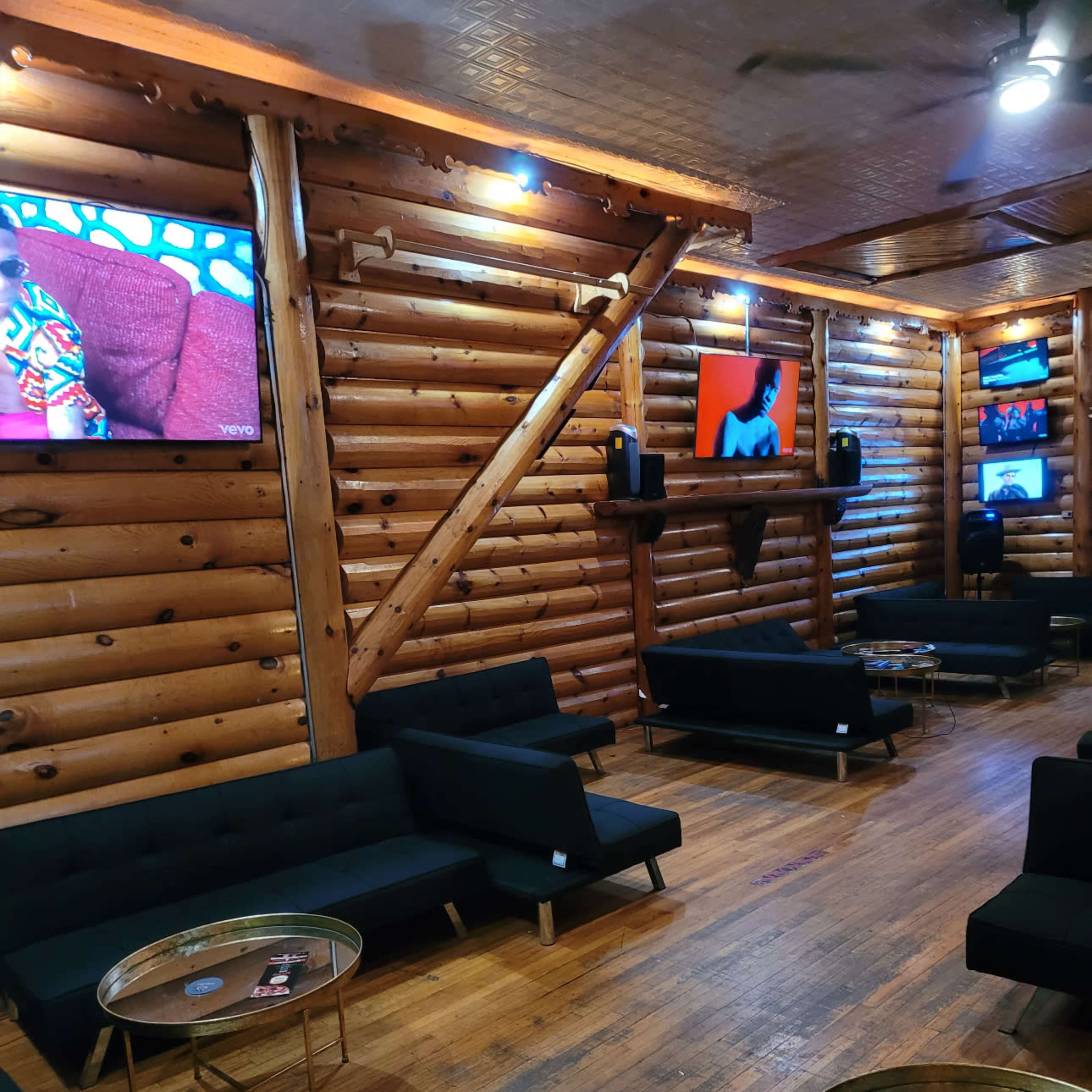 The interior features a cozy lounge with wooden walls, black couches, and several televisions mounted on the walls.