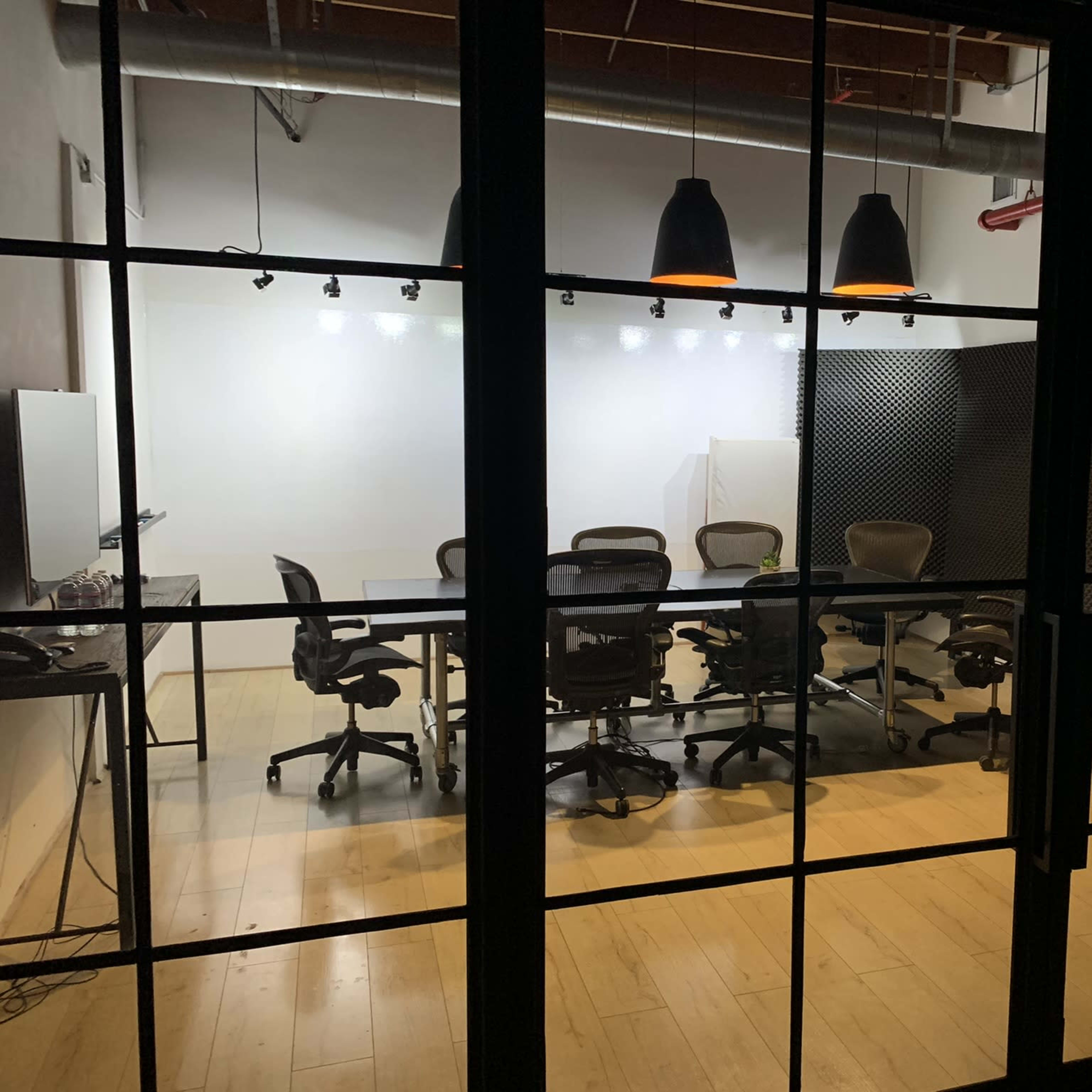 A conference room with a large table and several office chairs is visible through glass doors, featuring acoustic paneling on the walls and overhead lighting.