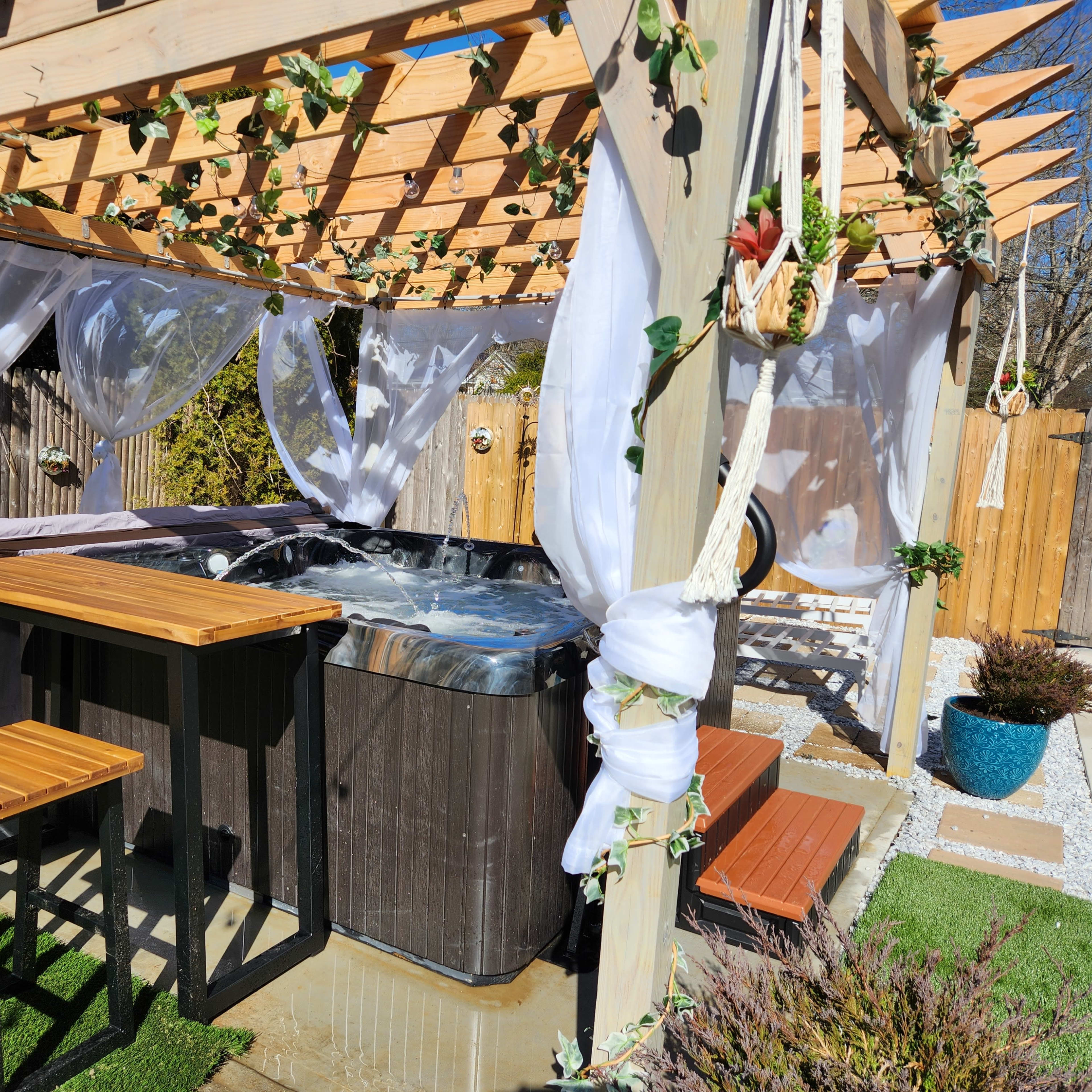 A spa area with a hot tub surrounded by wooden structures and tables, decorated with white drapes and greenery.