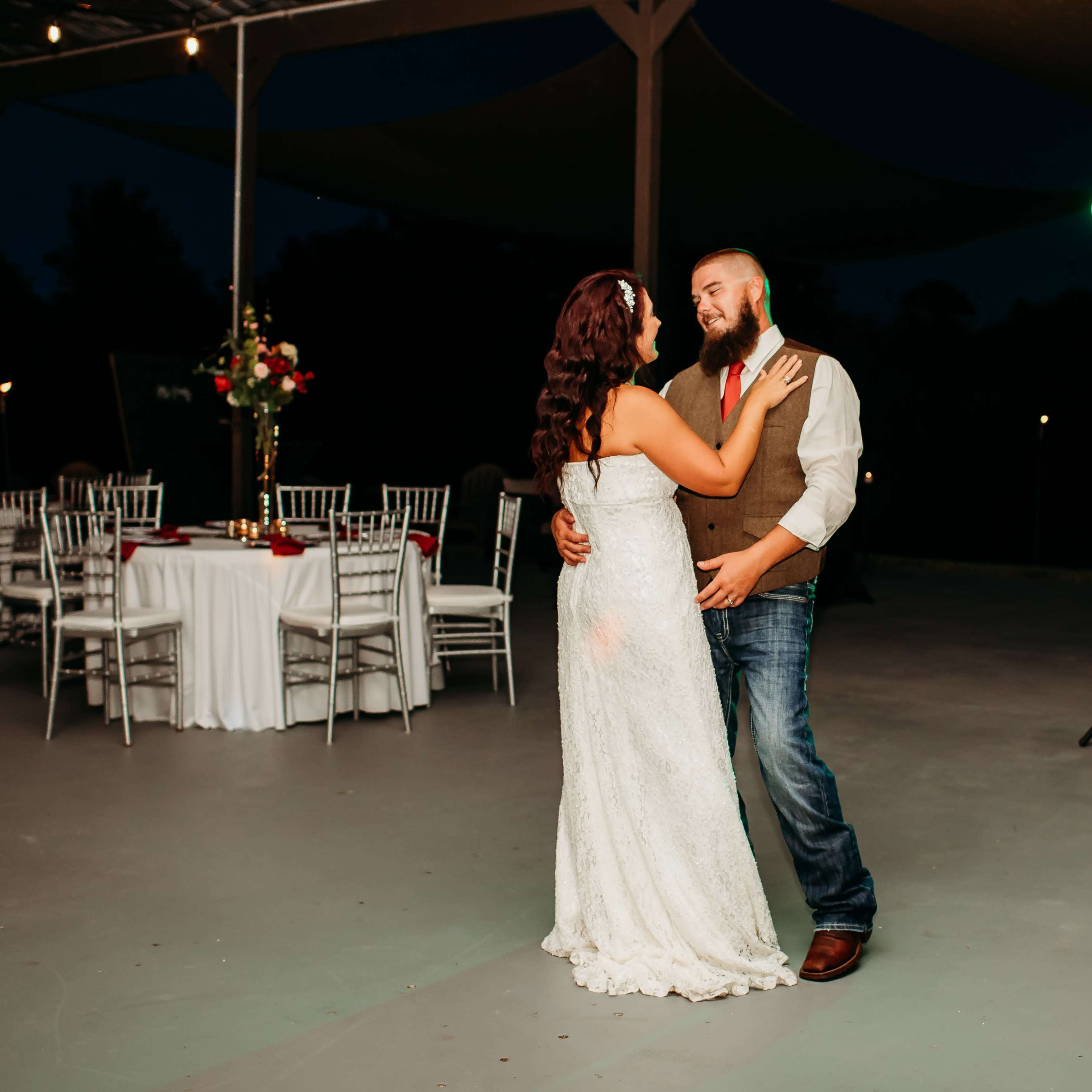 A couple dances closely on an outdoor patio, surrounded by elegantly set tables and soft lighting.