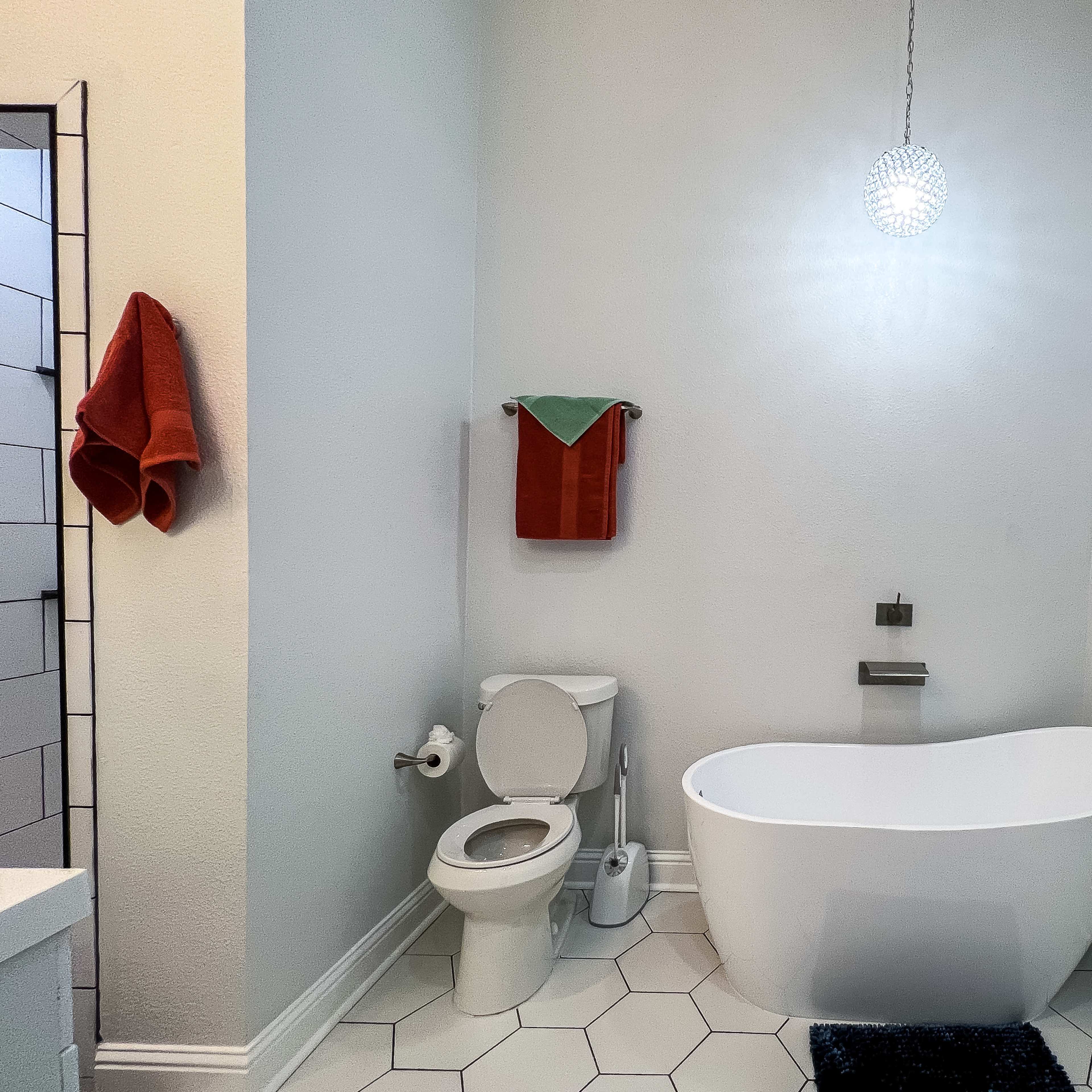 A modern bathroom featuring a freestanding tub, a toilet, a wall-mounted faucet, and a pendant light, with neatly arranged towels on a rack.