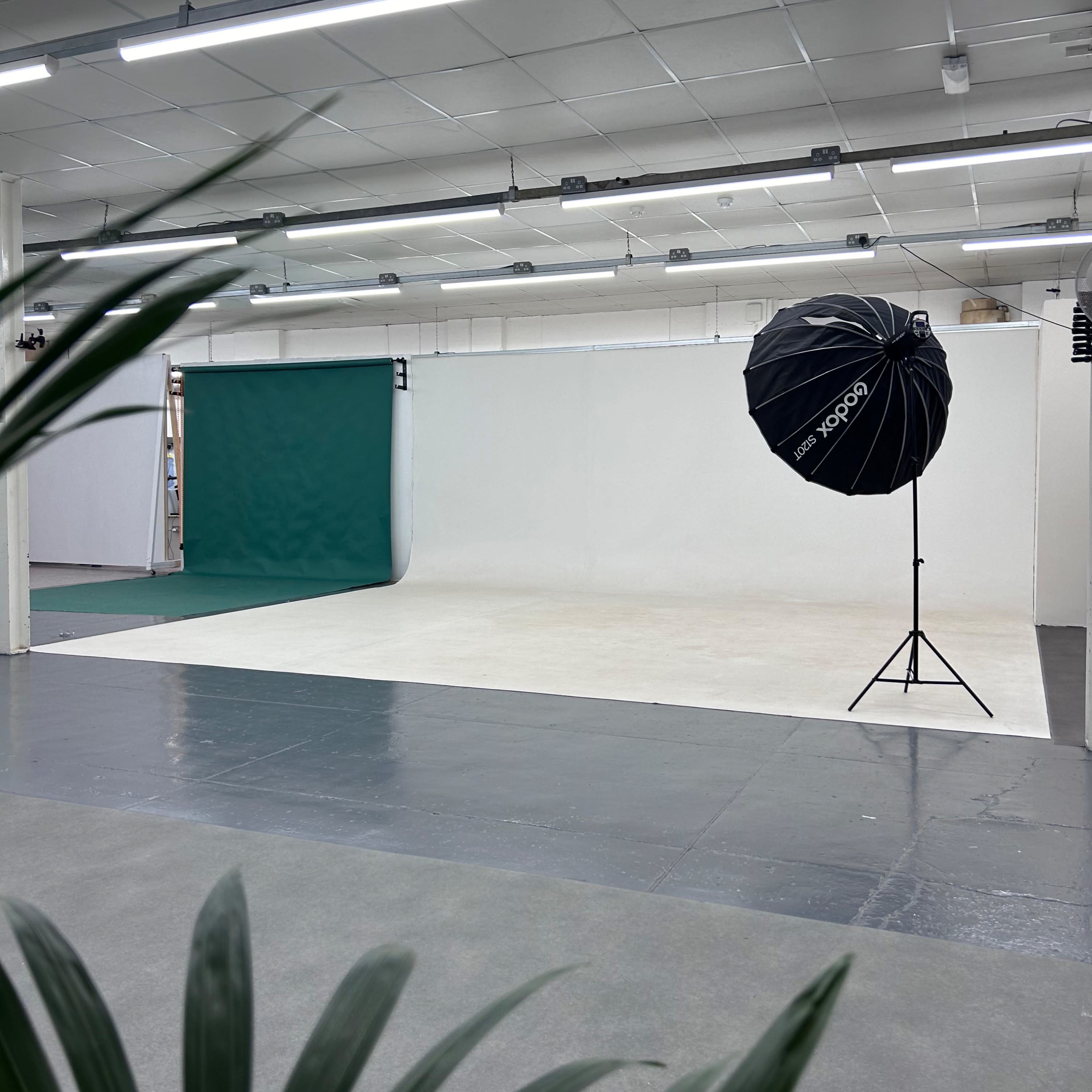 A photography studio featuring a green backdrop, white walls, and a large softbox on a stand.