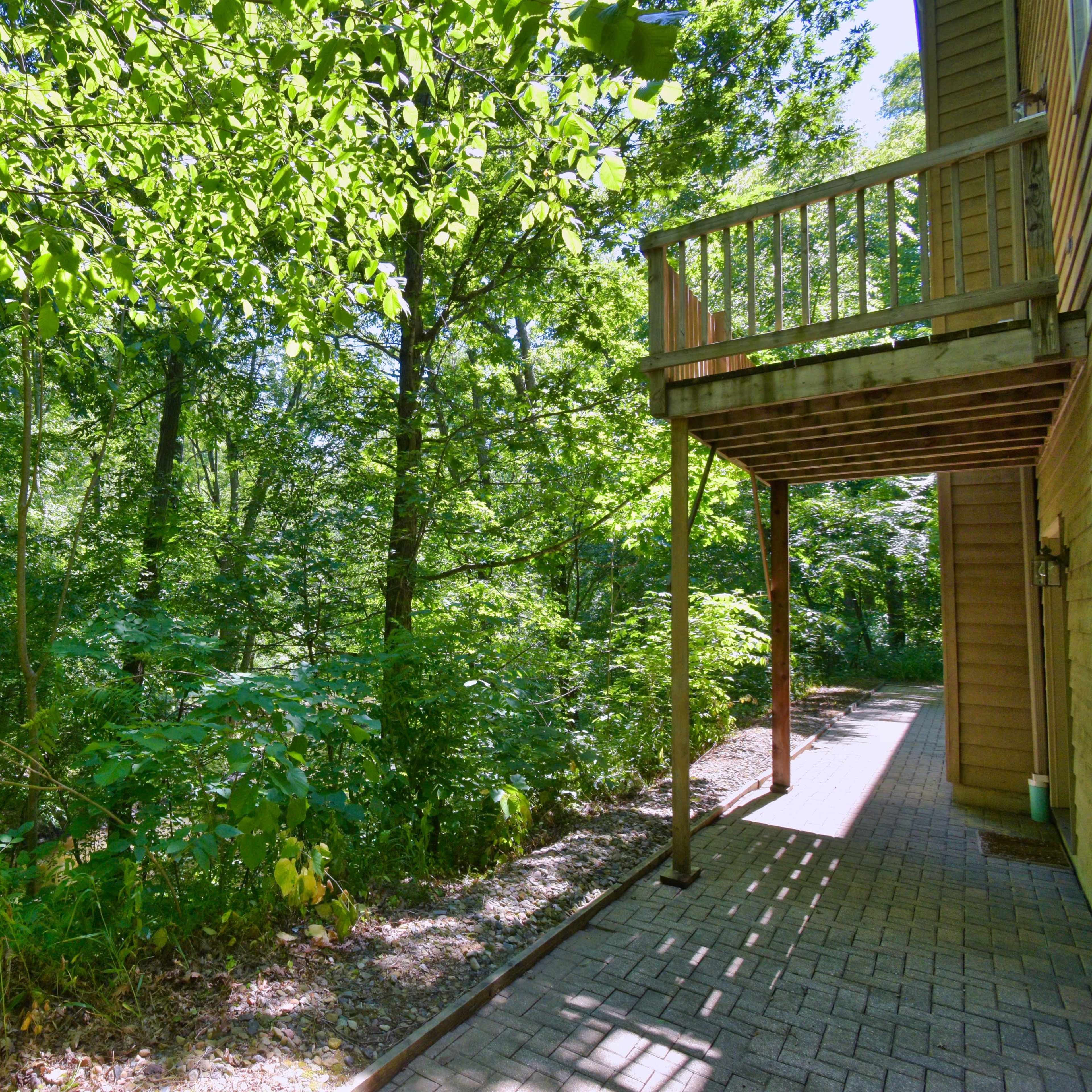 A wooden deck extends from a house, surrounded by dense greenery and trees.
