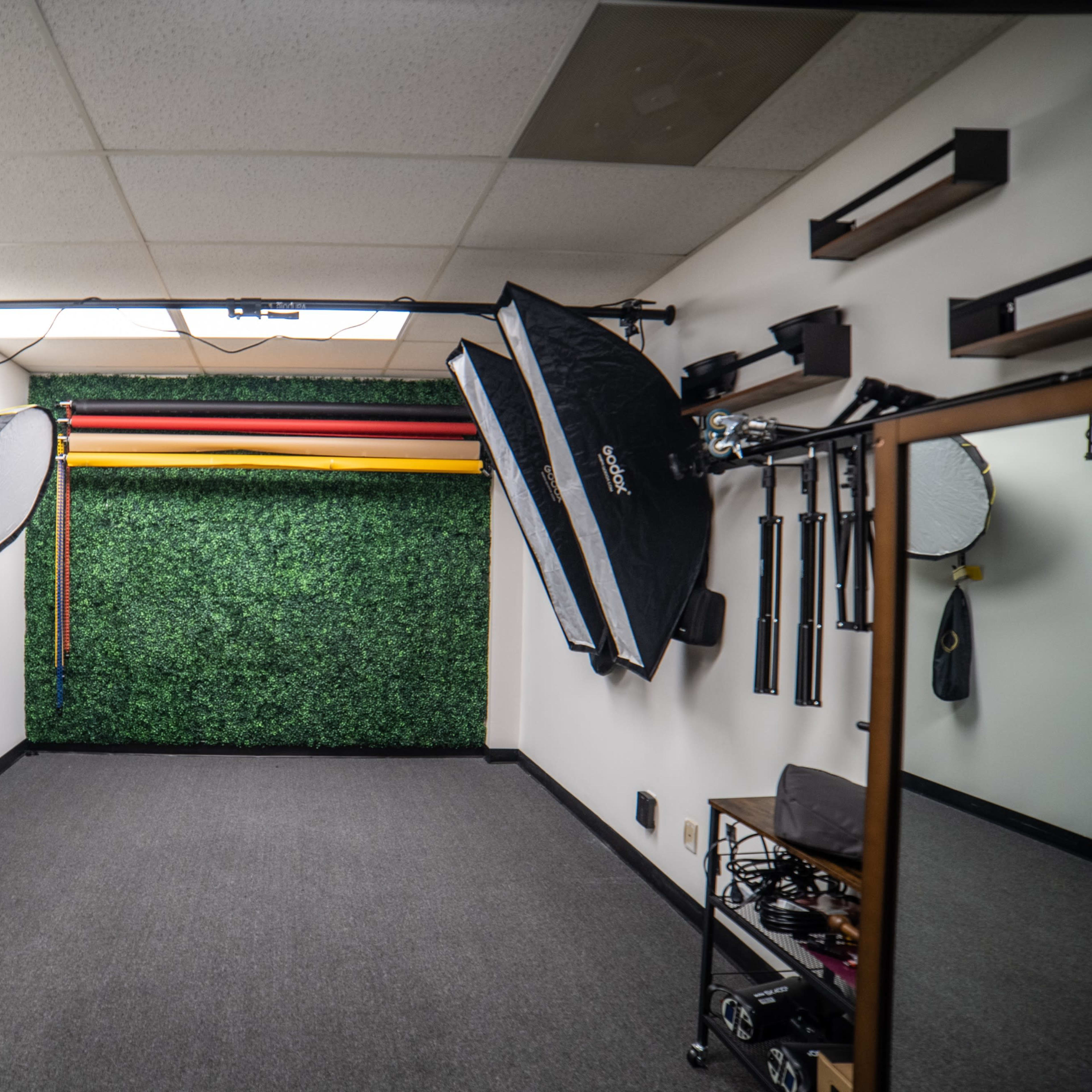 A photography studio with a green foliage backdrop, lighting equipment, and various props arranged along the walls.