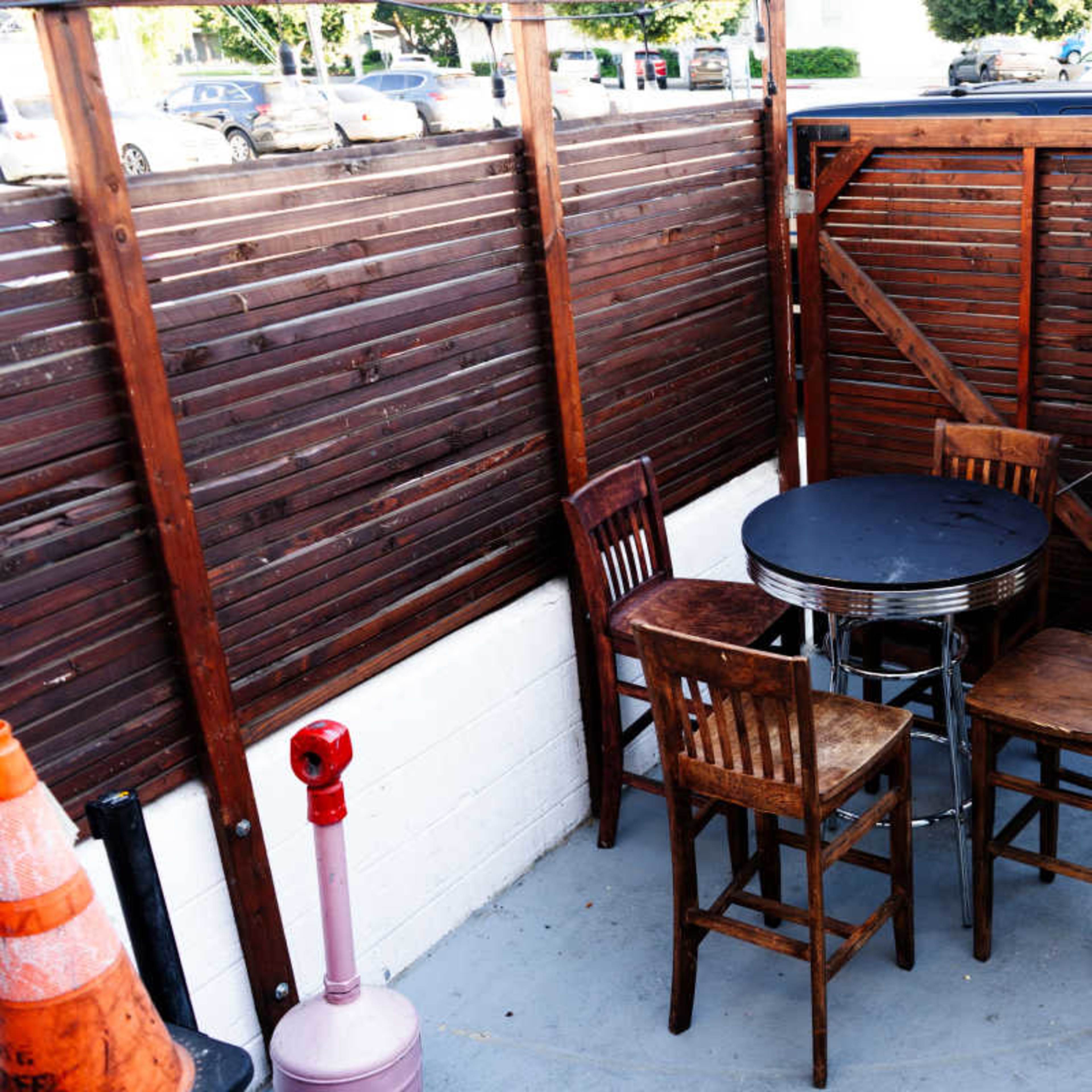 A small outdoor seating area with a round black table and four wooden chairs enclosed by wooden slatted walls.