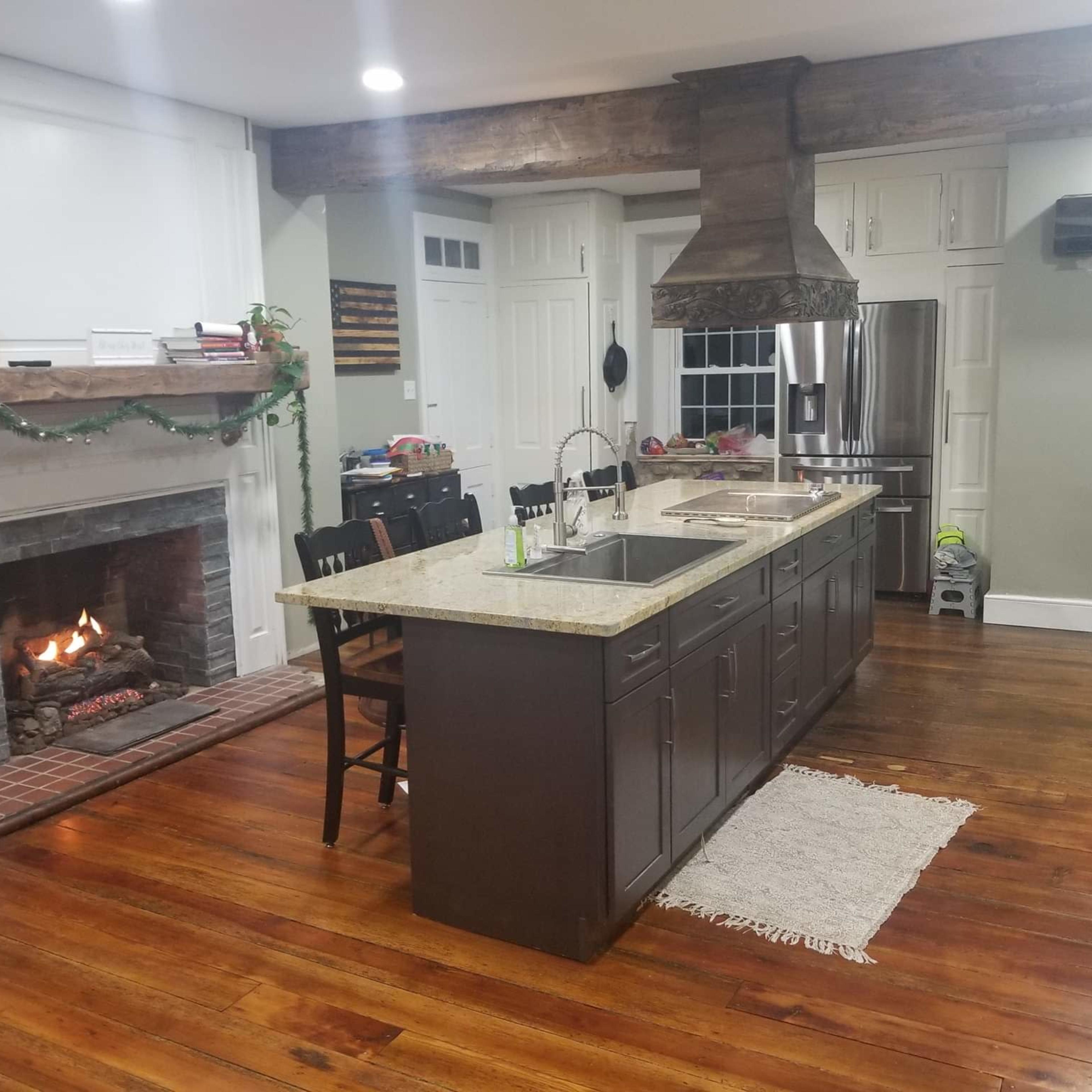 The kitchen features an island with dark cabinetry, a large hood over the stovetop, and a fireplace to the side, all set on polished wood flooring.