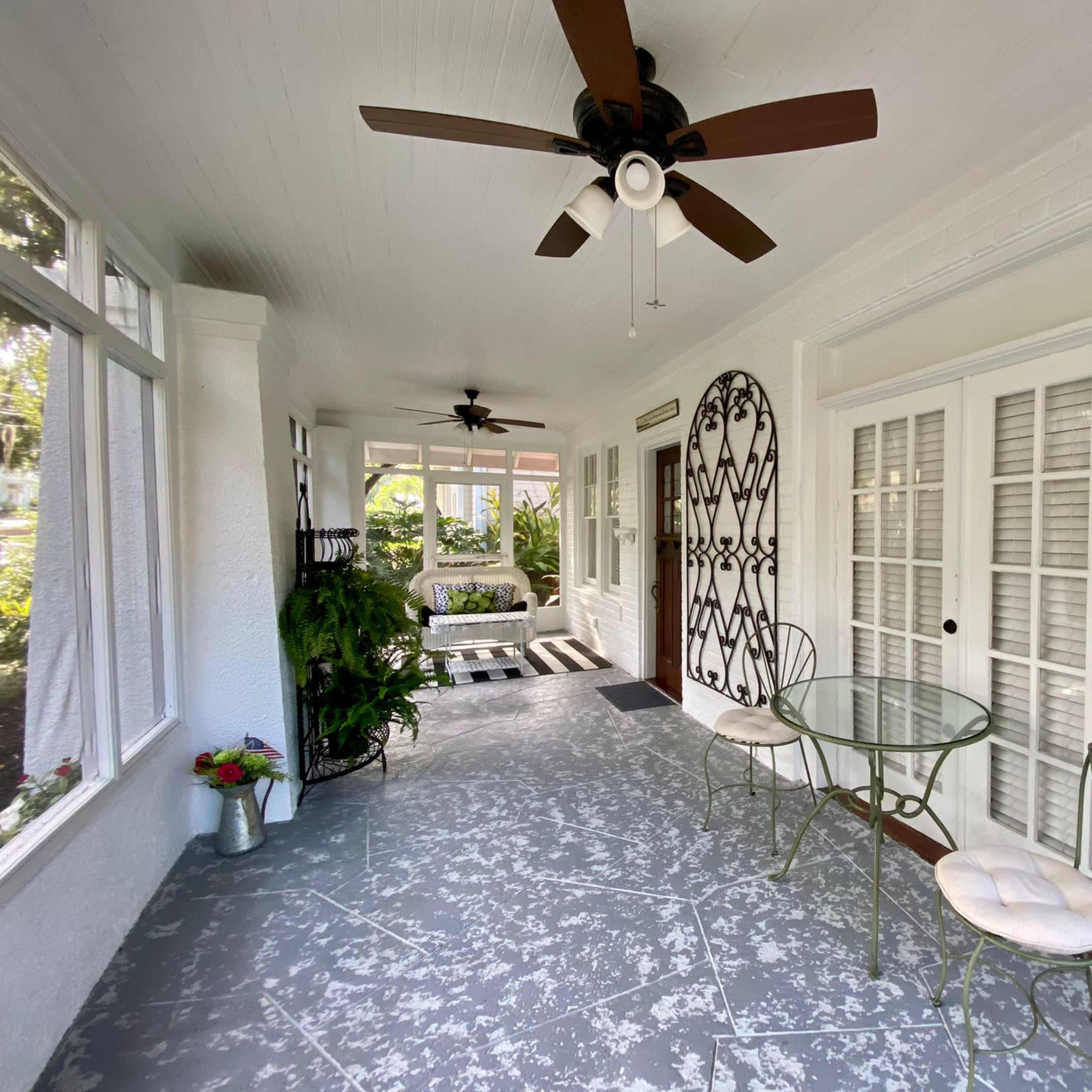 A covered porch featuring a small table with two chairs, ceiling fans, and decorative elements on the walls.