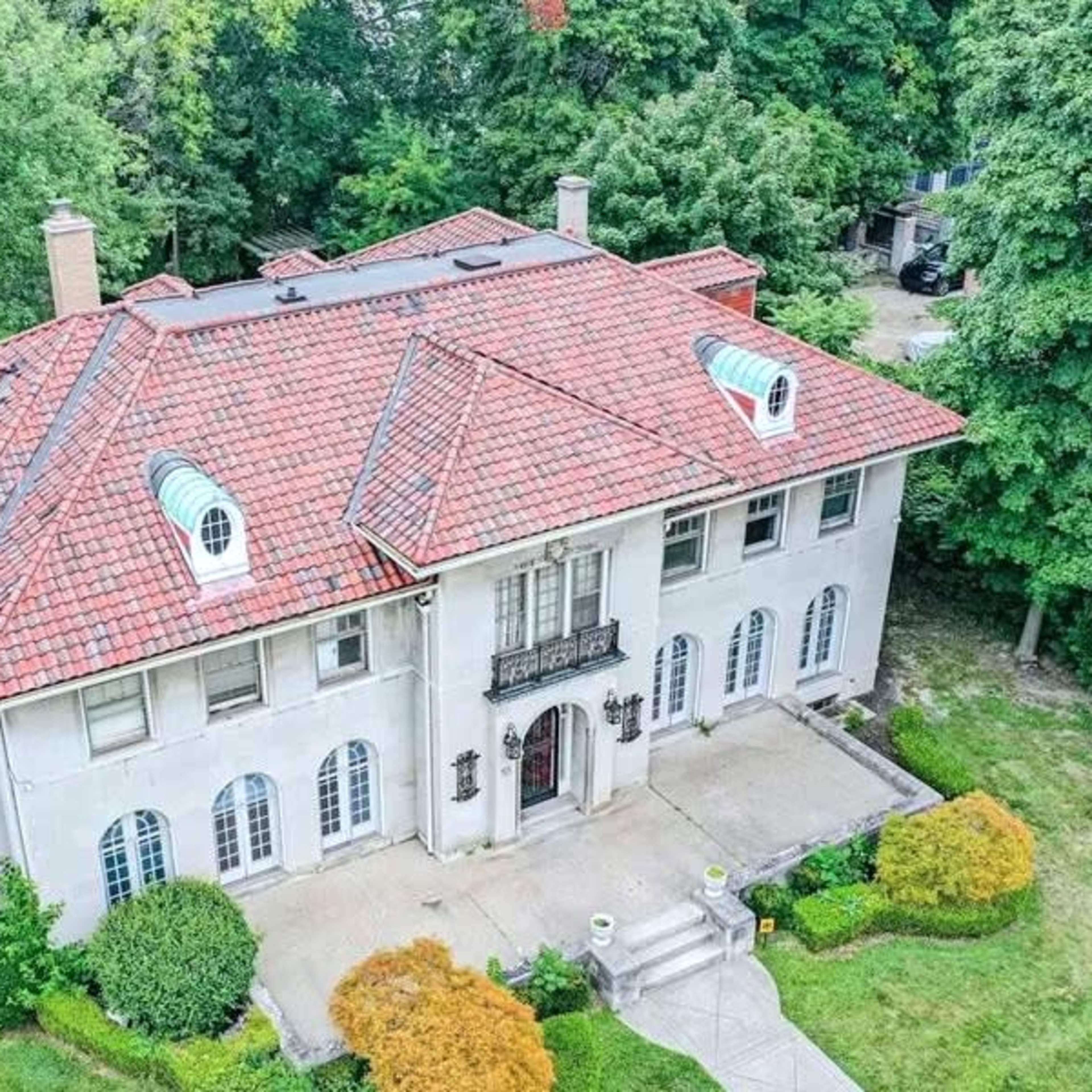 A large, two-story house with a red tiled roof, surrounded by greenery and a landscaped yard.