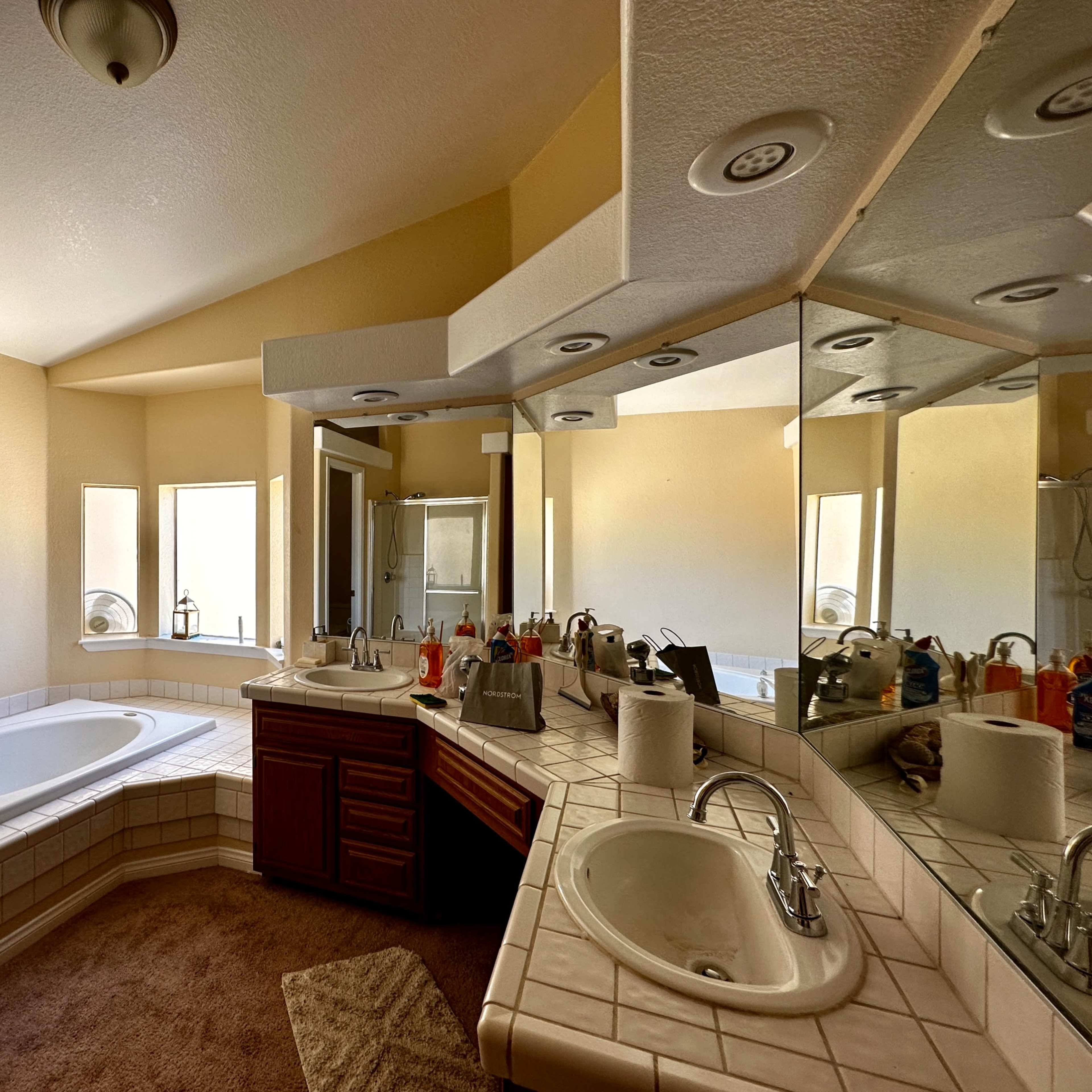 A spacious bathroom features a large corner bathtub, dual sinks with a vanity, and multiple mirrors reflecting the room's layout.