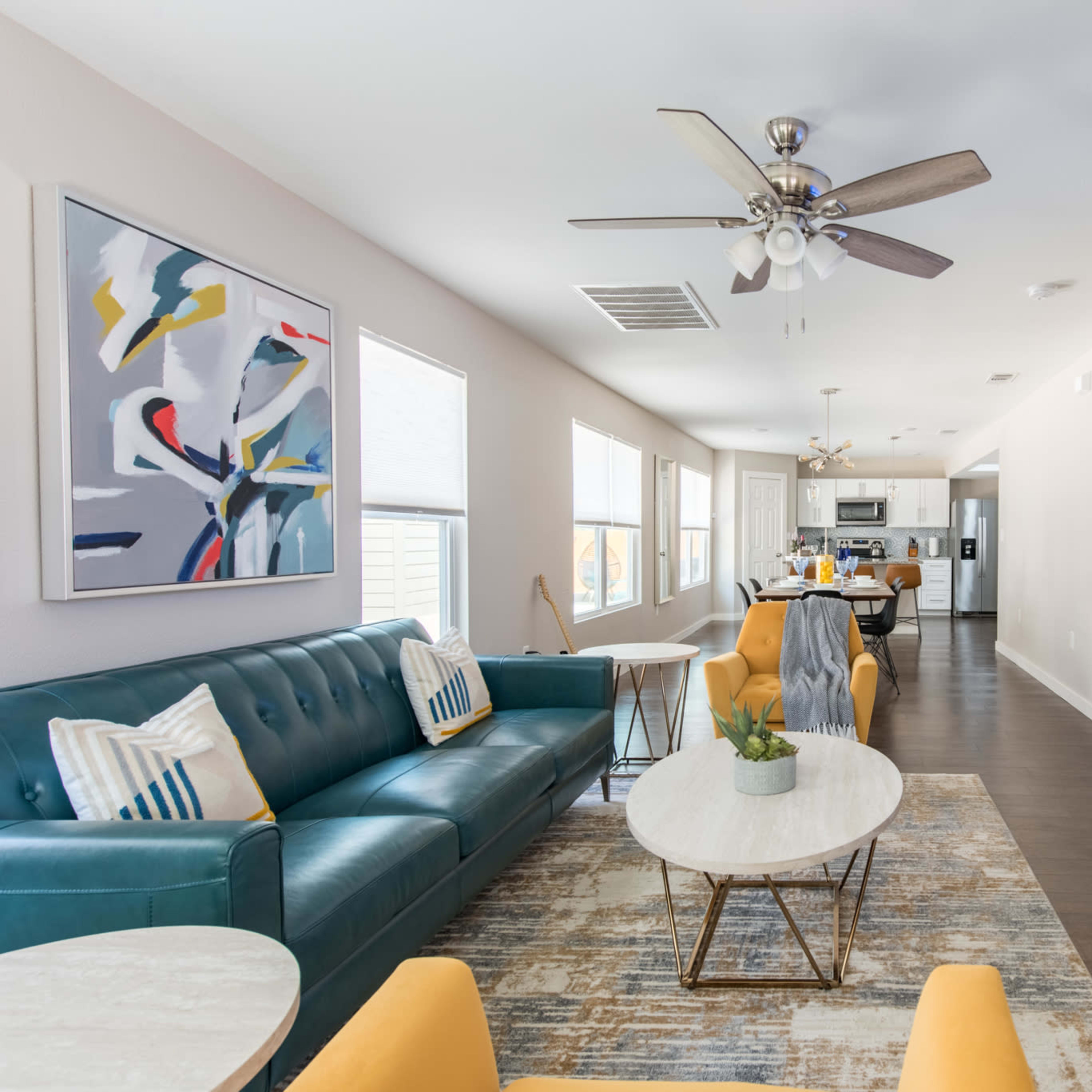 A modern living room with a teal sofa, a marble coffee table, and a large wall-mounted TV, adjacent to a kitchen visible in the background.